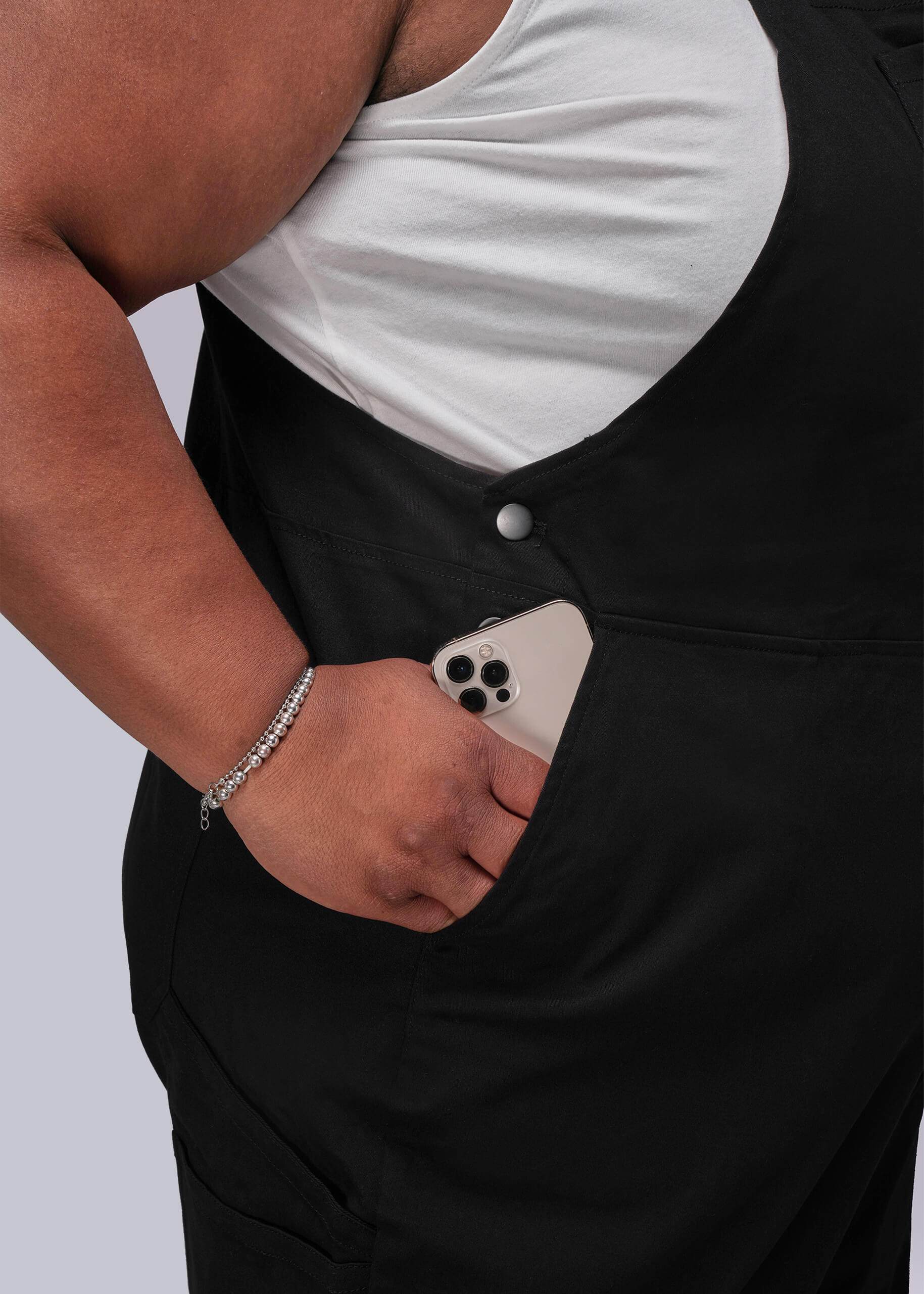 1X=Person wearing black overalls with a white shirt underneath, holding a phone in their pocket.