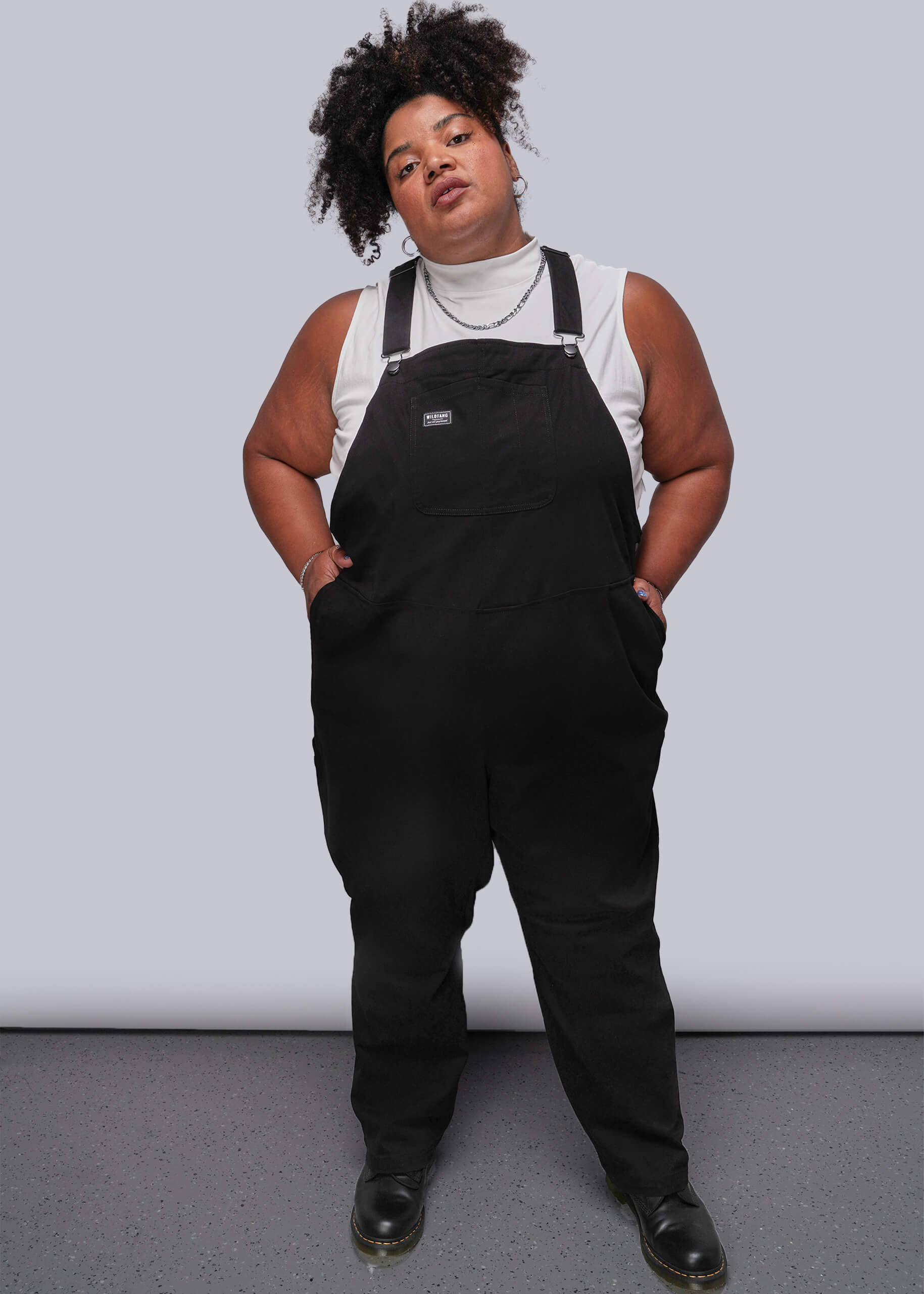 1X=Person wearing black overalls against a plain background