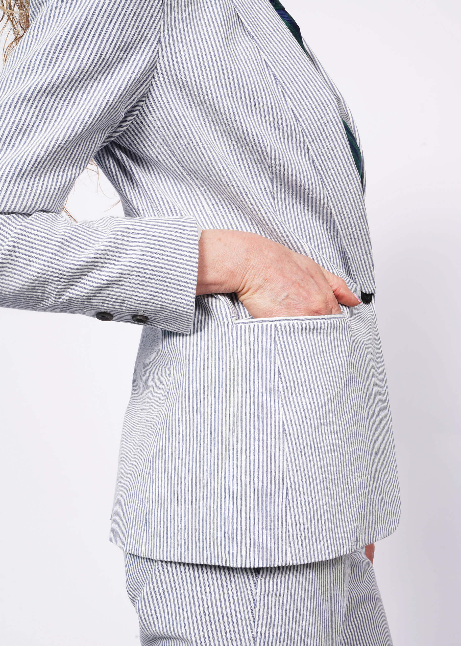 S= Close up of side view of person wearing seersucker blue and white blazer with matching seersucker trousers.
