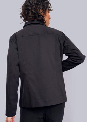 S=A person with curly hair, wearing The Essential Utility Jacket and facing away from the camera, stands against a plain white background. This black jacket offers stretch comfort and features deep pockets for extra functionality.