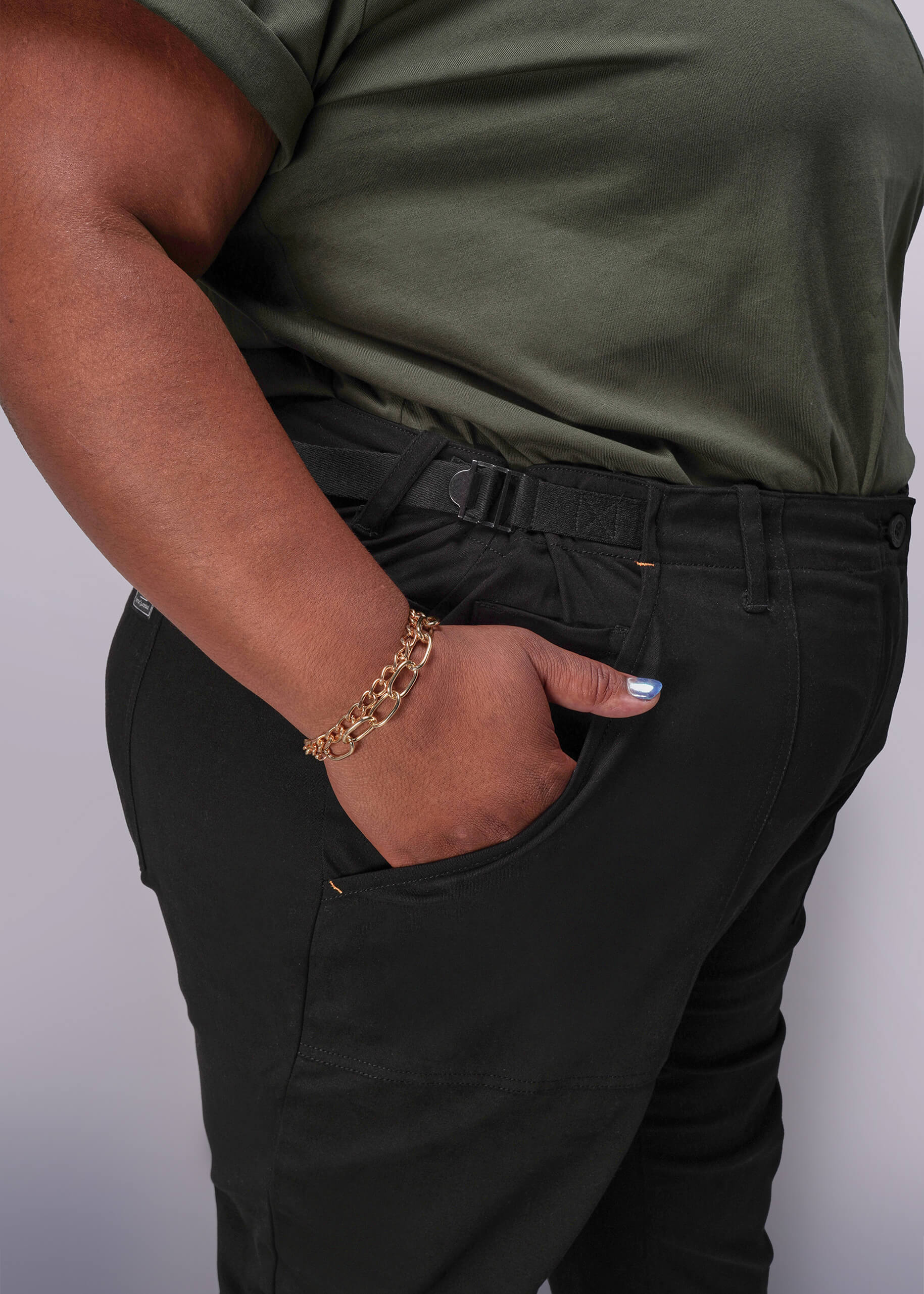 1X=Person wearing a green shirt and black pants with a gold bracelet on a plain background