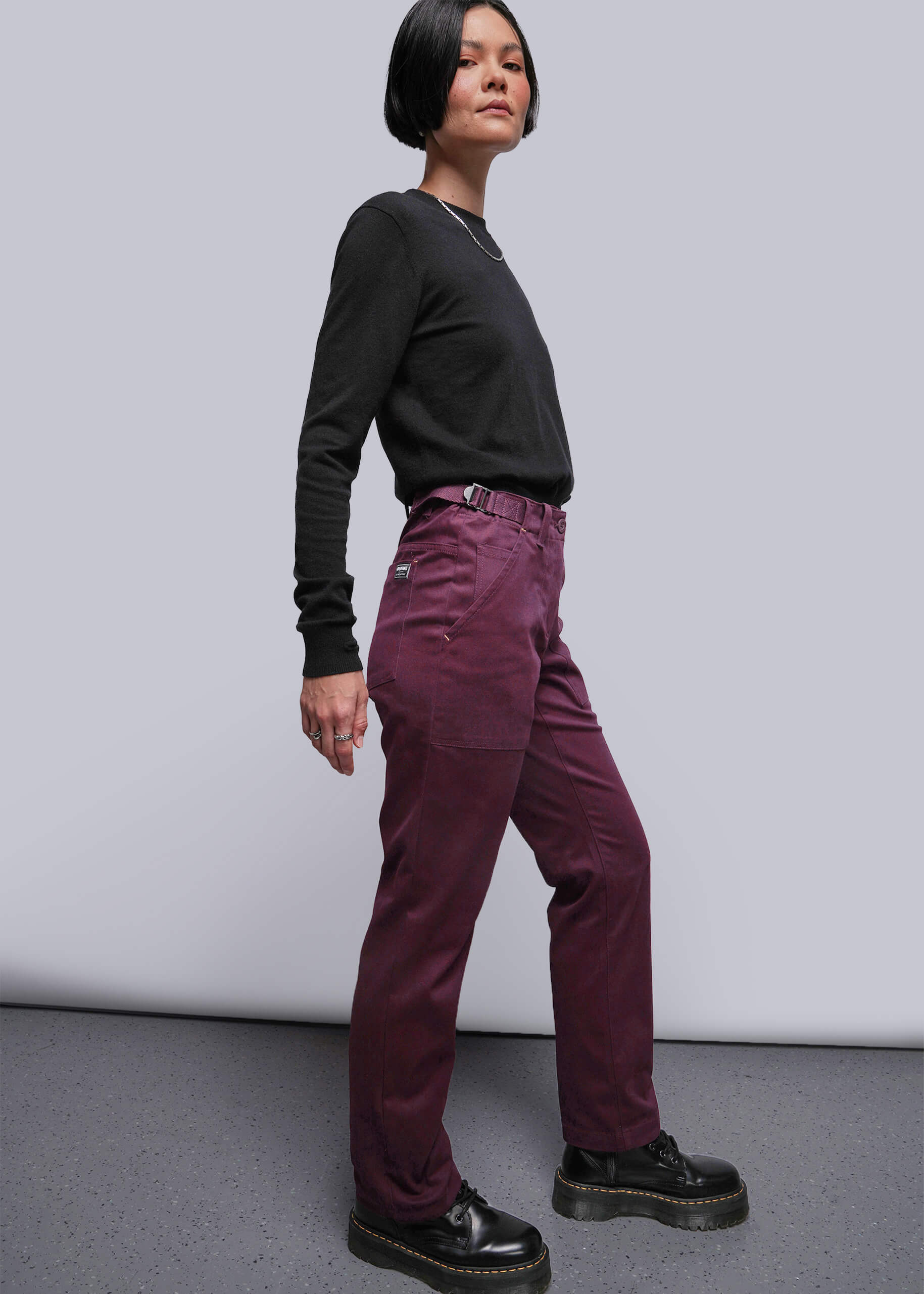 S=Person wearing a black long-sleeve shirt and maroon pants against a plain background