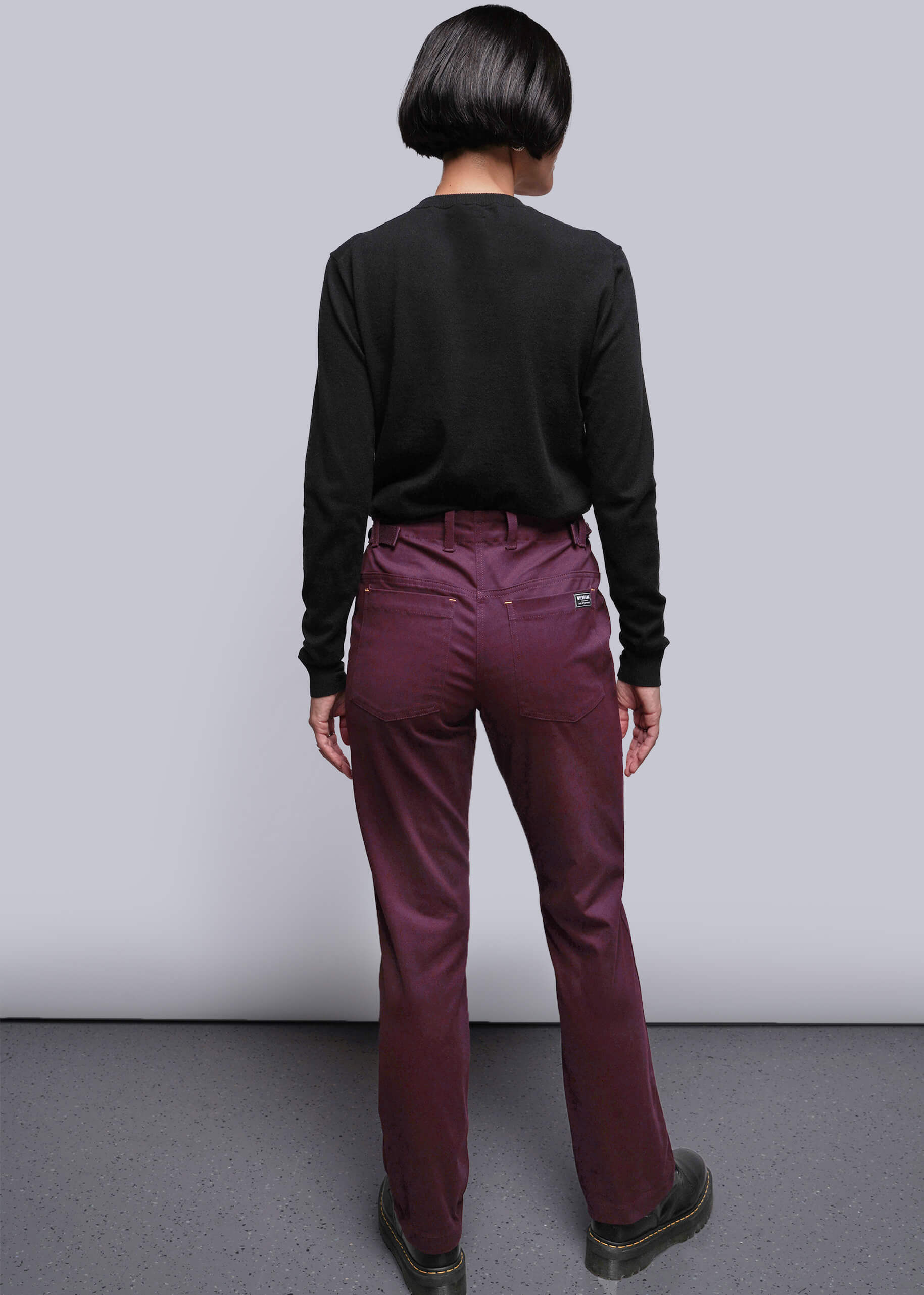 S=Person wearing a black long-sleeve shirt and burgundy pants against a plain background