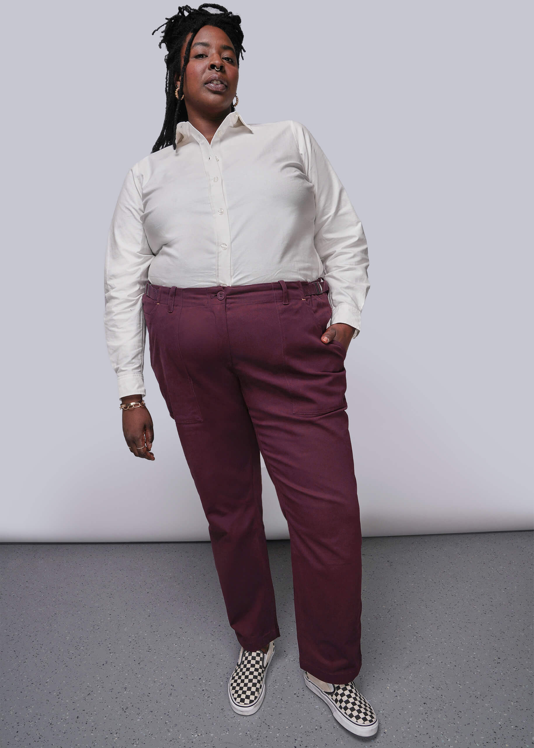 1X=Person wearing a white shirt and maroon pants with checkered shoes on a plain background