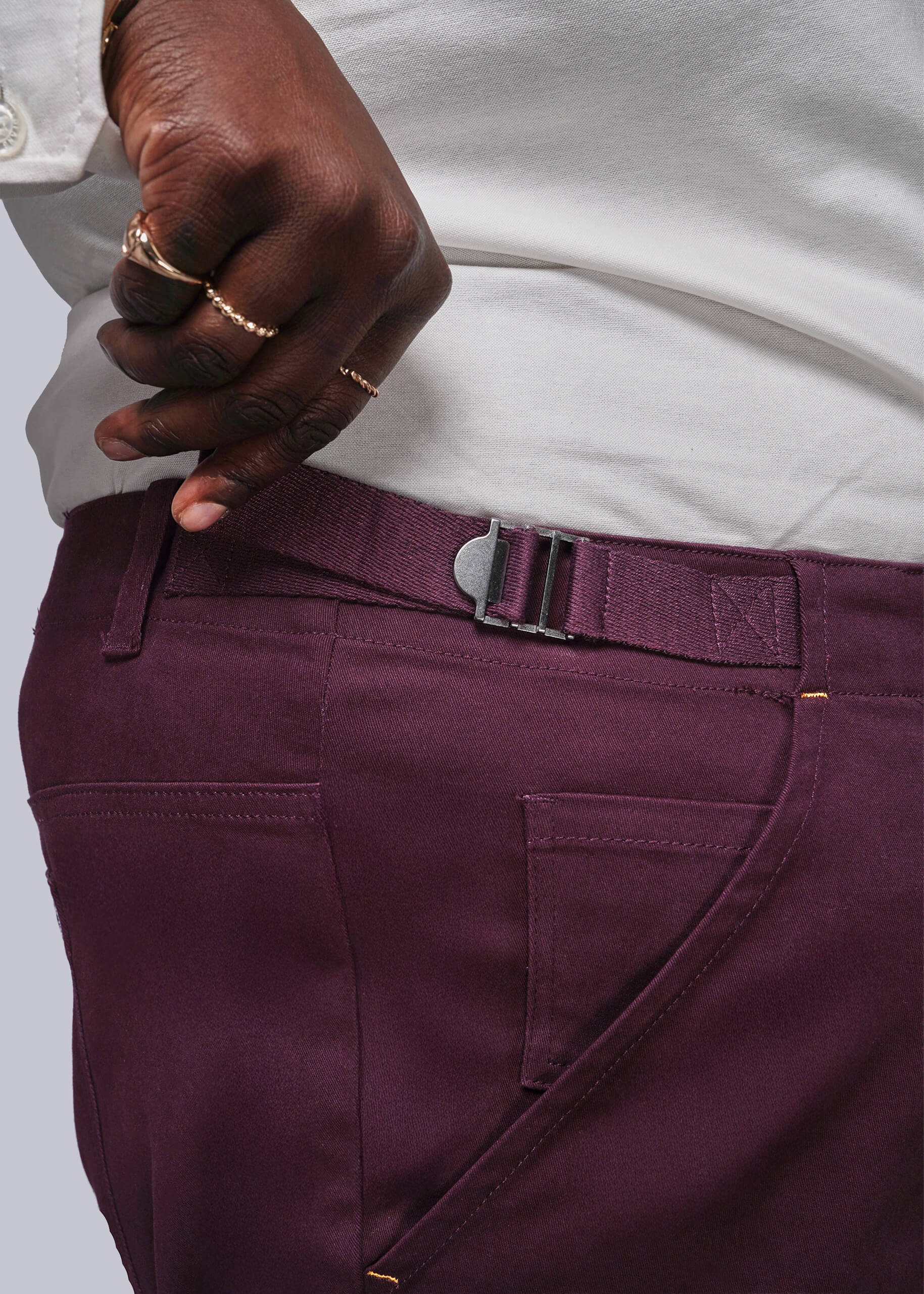 1X=Close-up of a person wearing purple pants with a white shirt and gold ring.