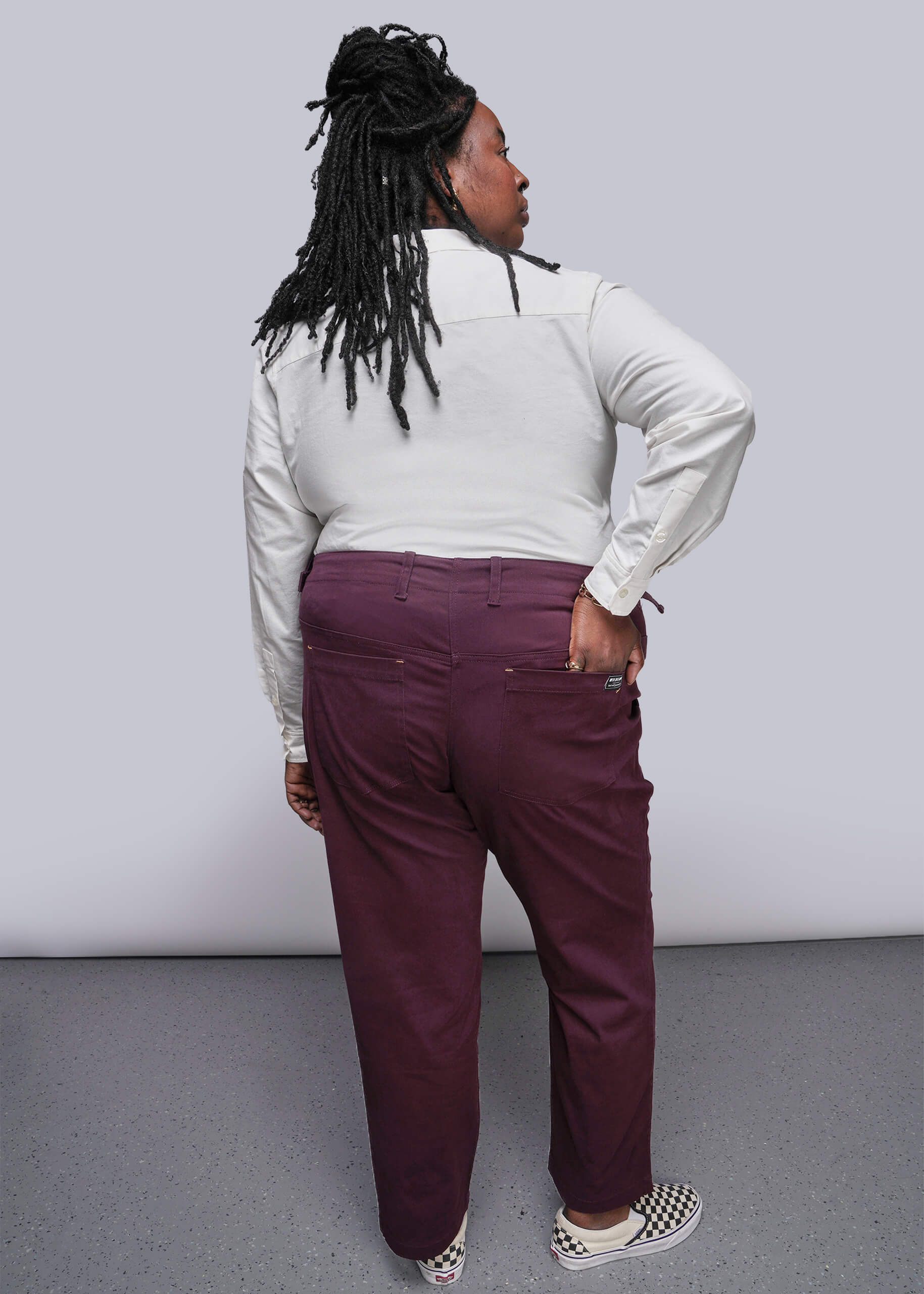 1X=Person wearing a white long-sleeve shirt and maroon pants against a plain background