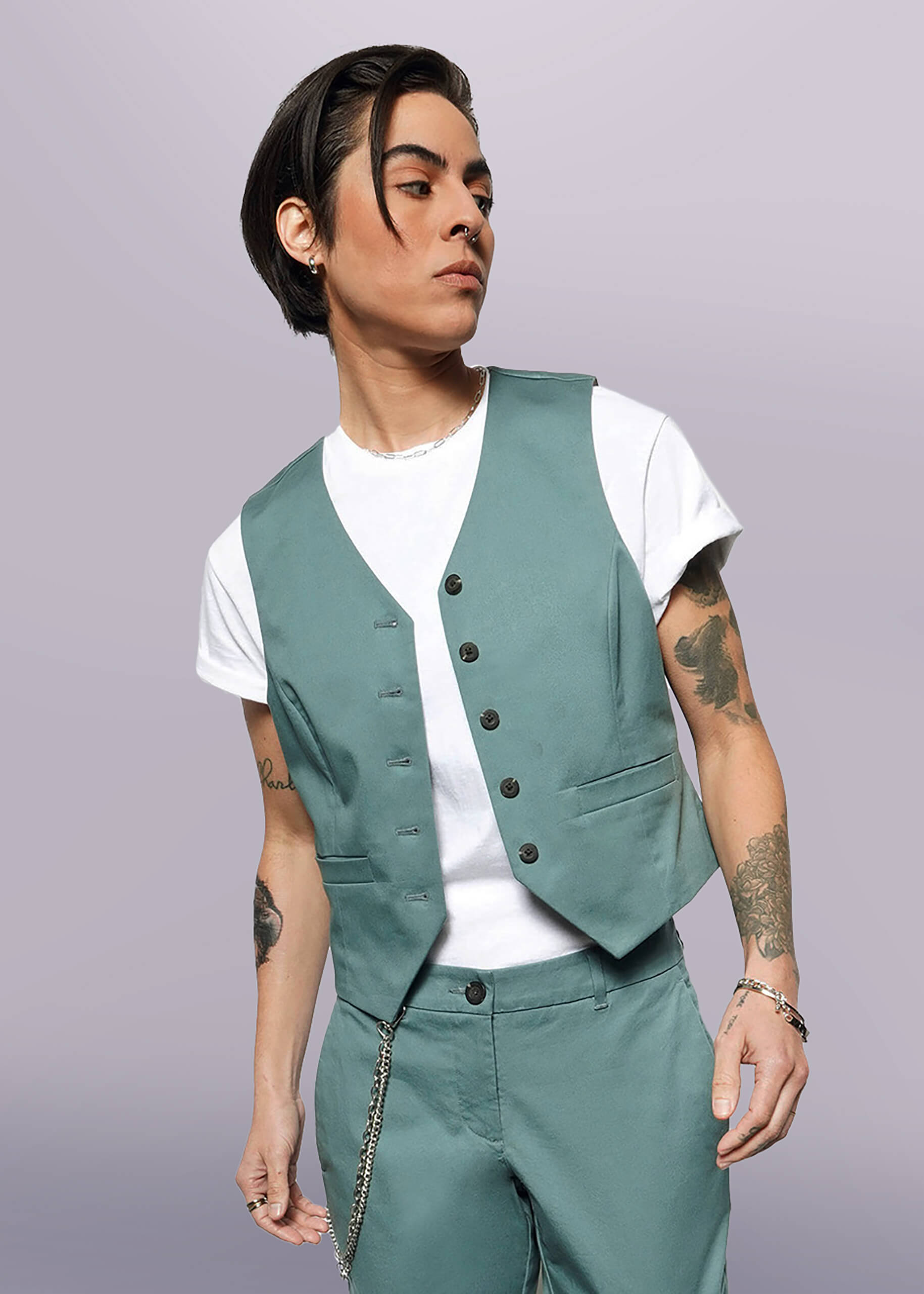 S= A person with short dark hair wears The Essential Vest and matching stretch cotton pants over a white t-shirt, accessorized with bracelets and a chain, standing against a plain white background.