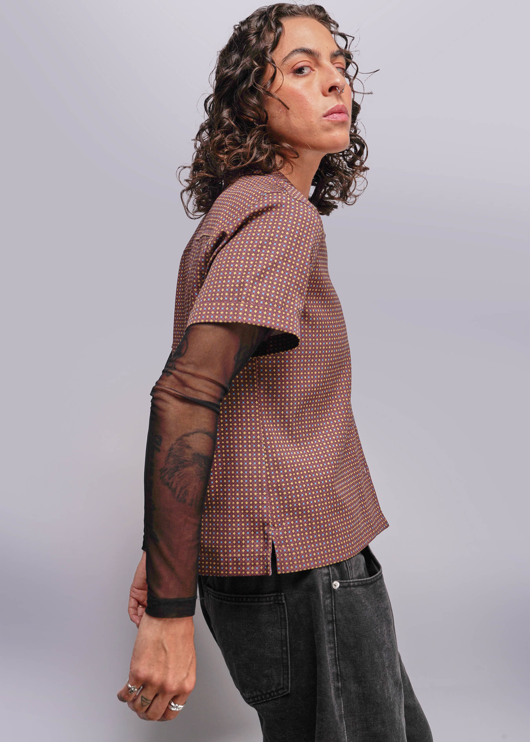 S=Person wearing a patterned top with sheer sleeves against a plain background
