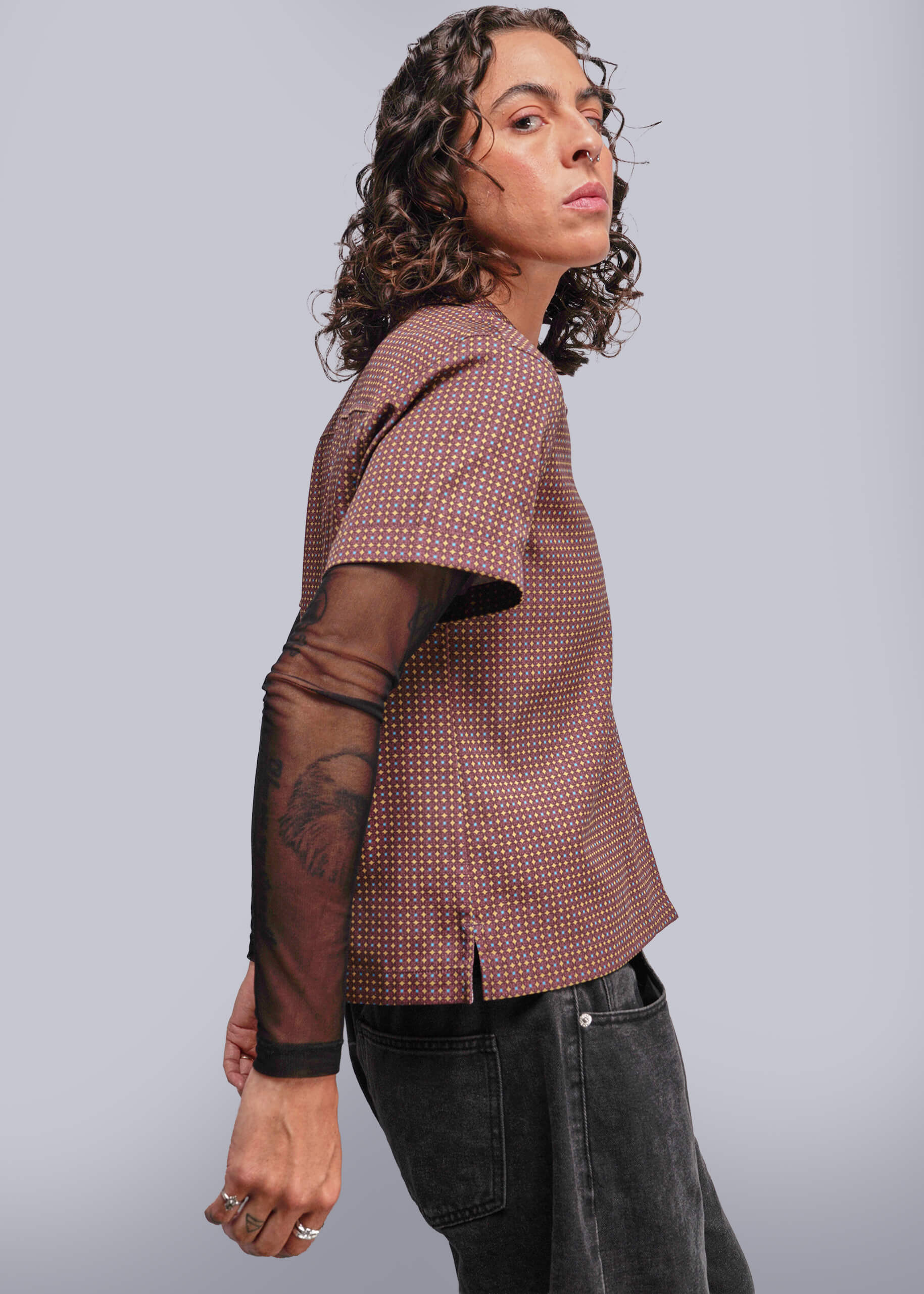 S=Person wearing a patterned top with sheer sleeves against a plain background