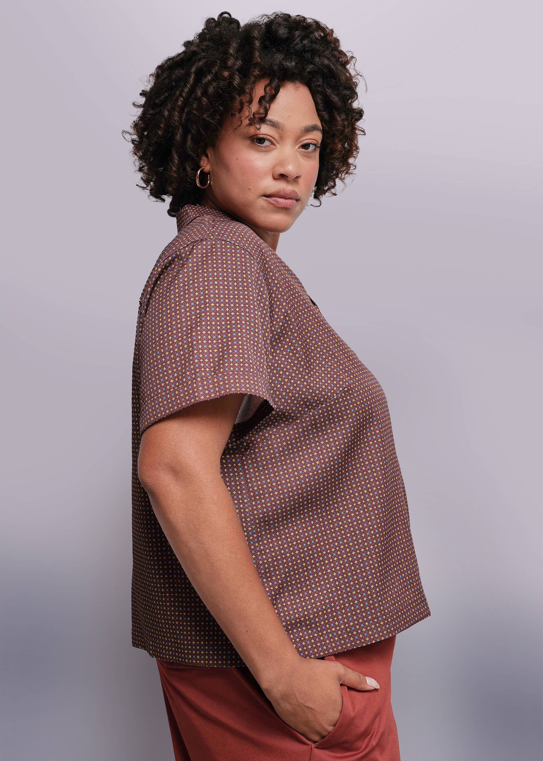 1X=Woman wearing a brown patterned shirt against a gray background