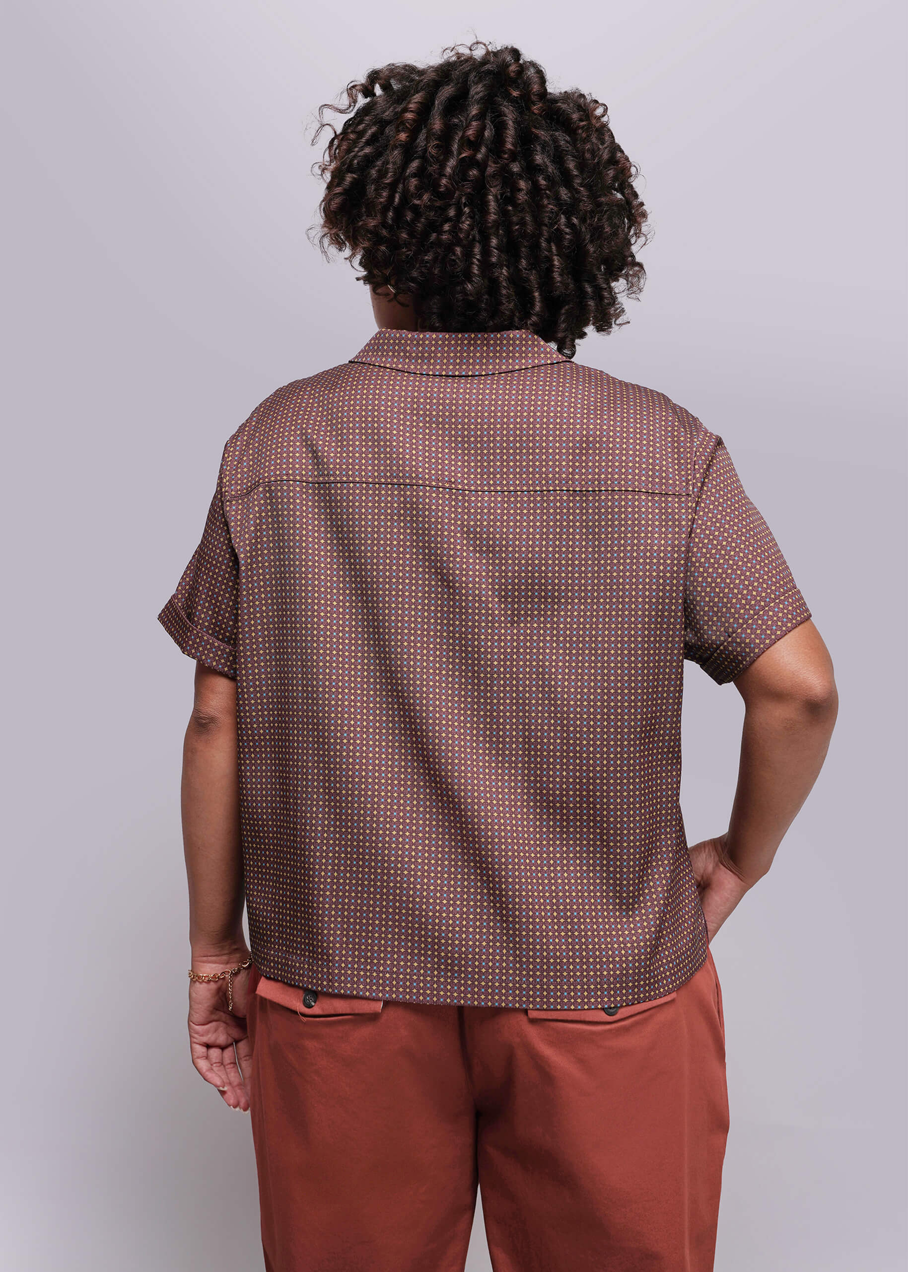 1X=Person wearing a patterned brown shirt and red pants against a plain background