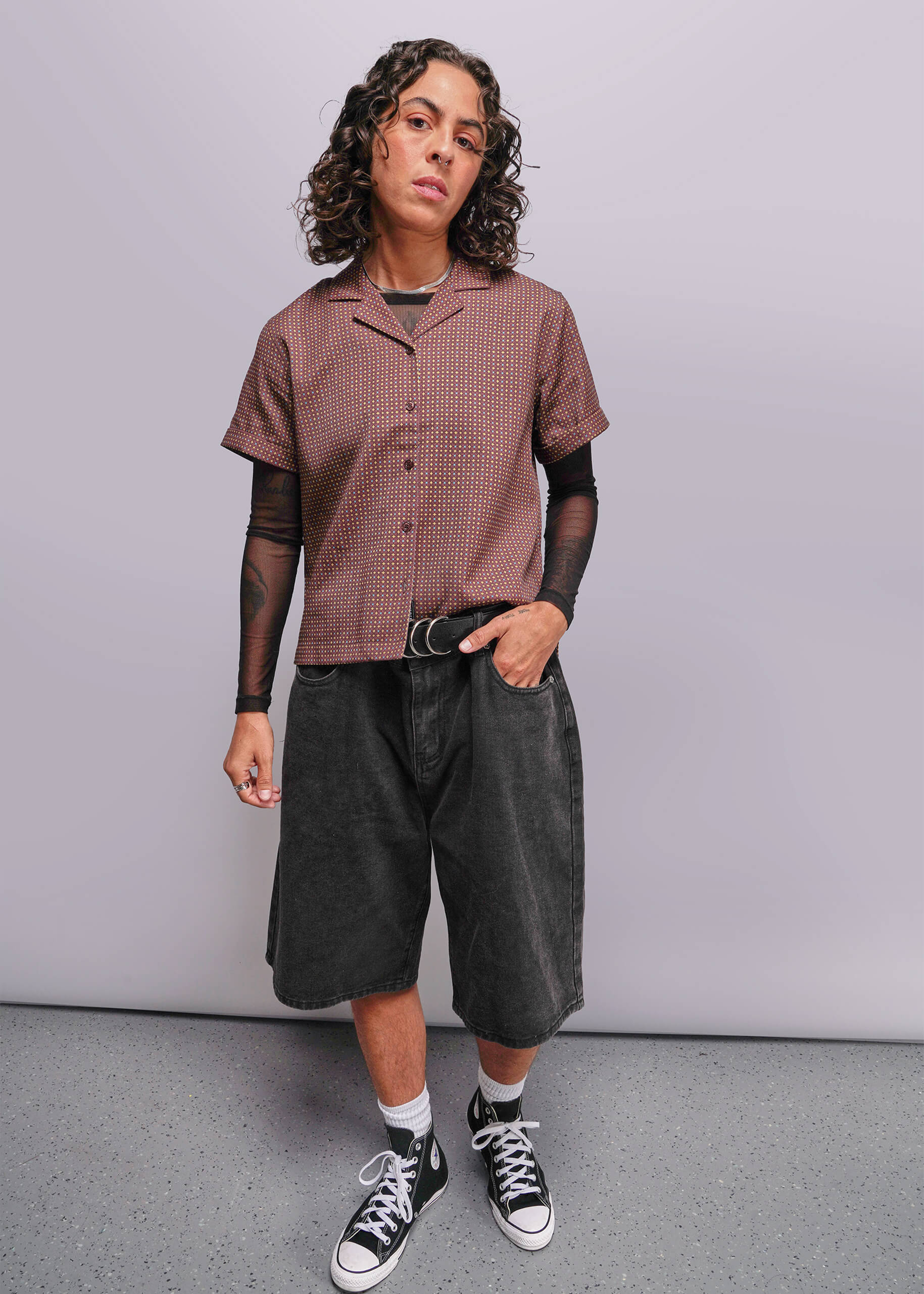 S=Person wearing a patterned shirt, dark shorts, and black sneakers on a plain background