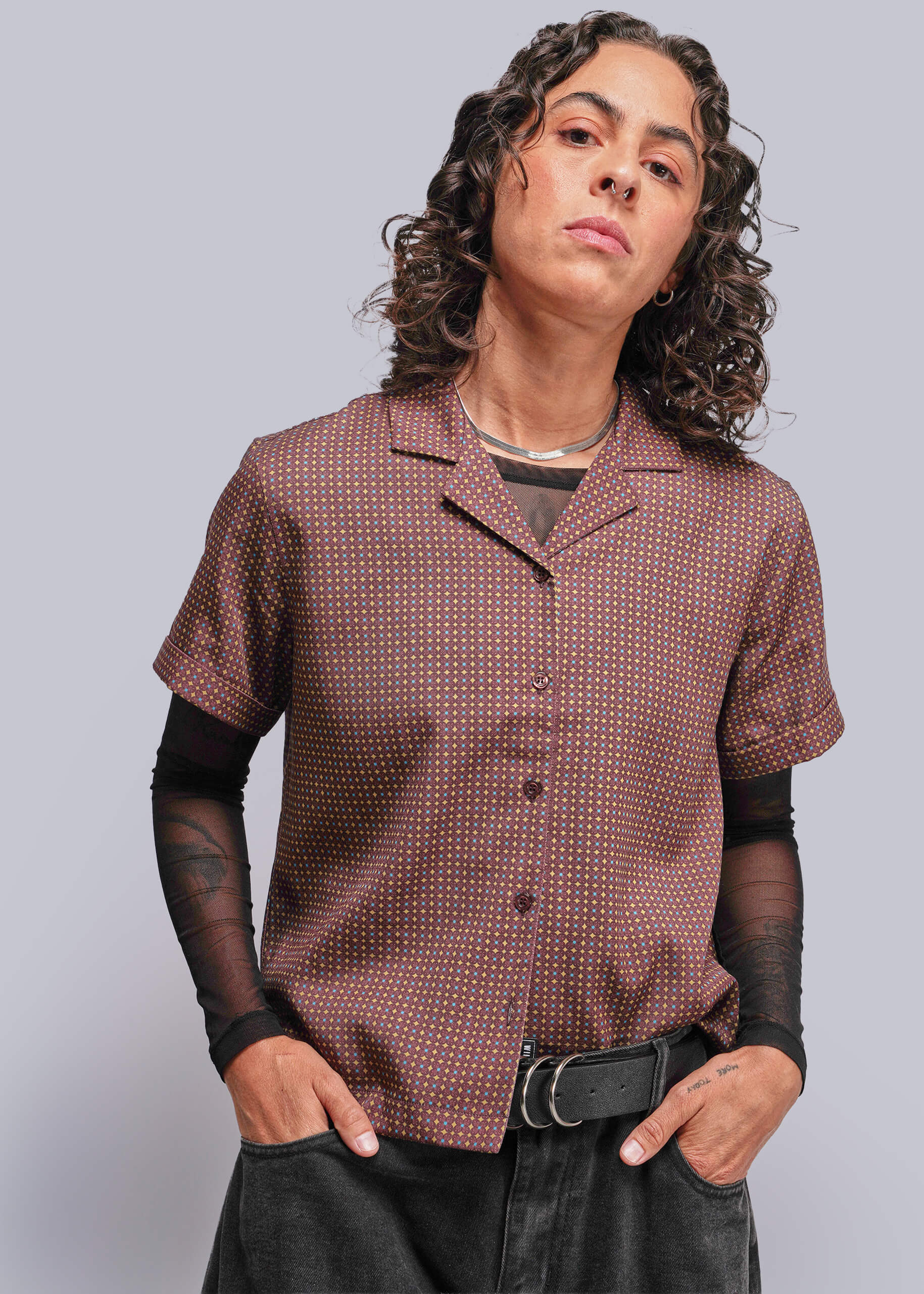 S=Person wearing a patterned brown shirt with black sleeves and pants against a plain background