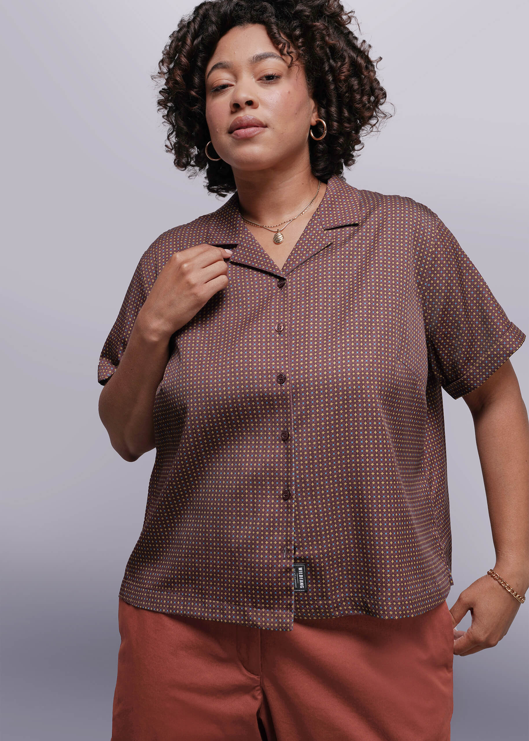 1X=Woman wearing a brown patterned button up against a plain background