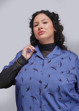 1X=Woman wearing a blue shirt with bird pattern against a gray background