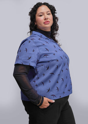 1X=Woman wearing a blue patterned shirt with black sleeves against a plain background