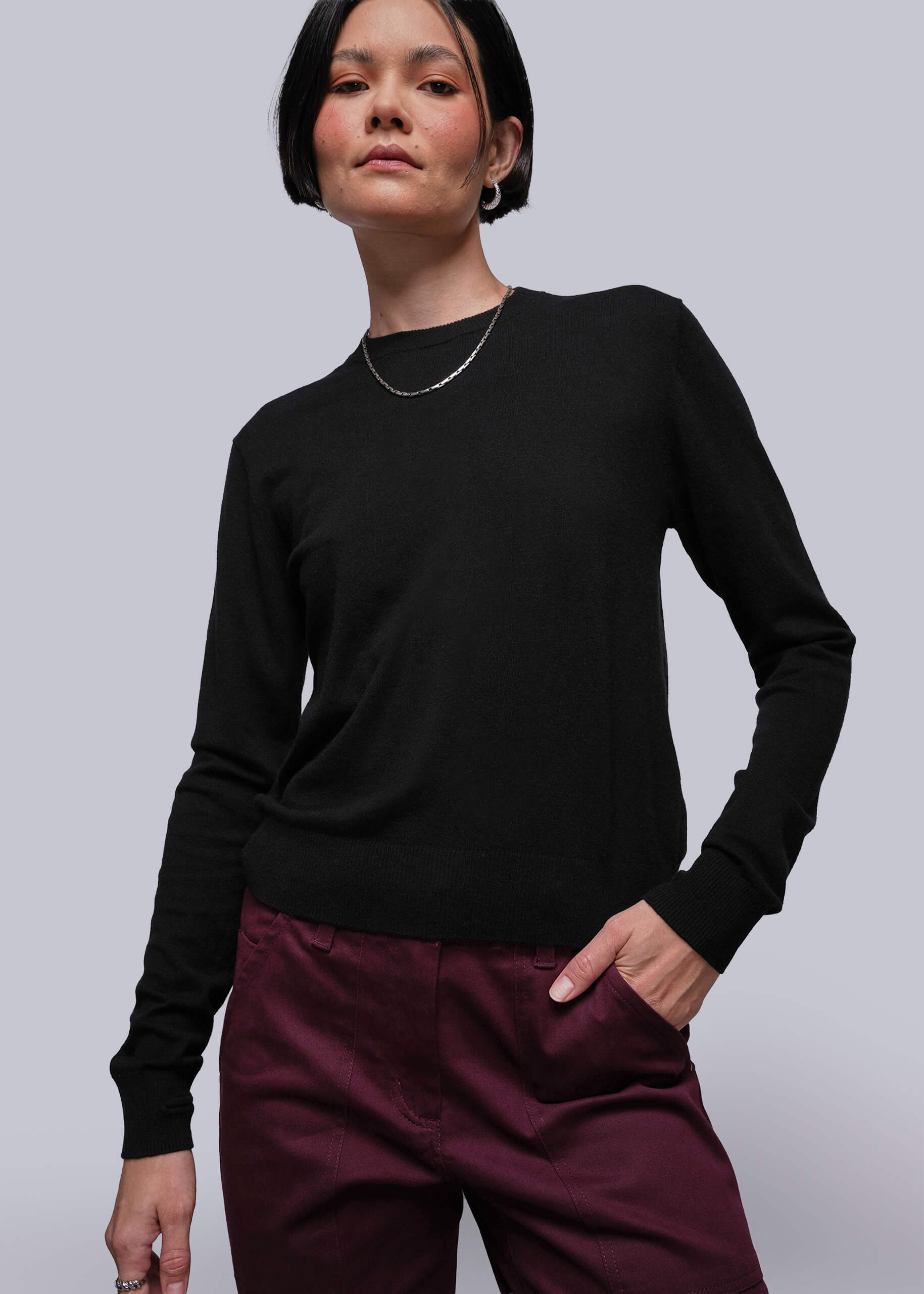 S=Person wearing a black long-sleeve top and burgundy pants against a light gray background