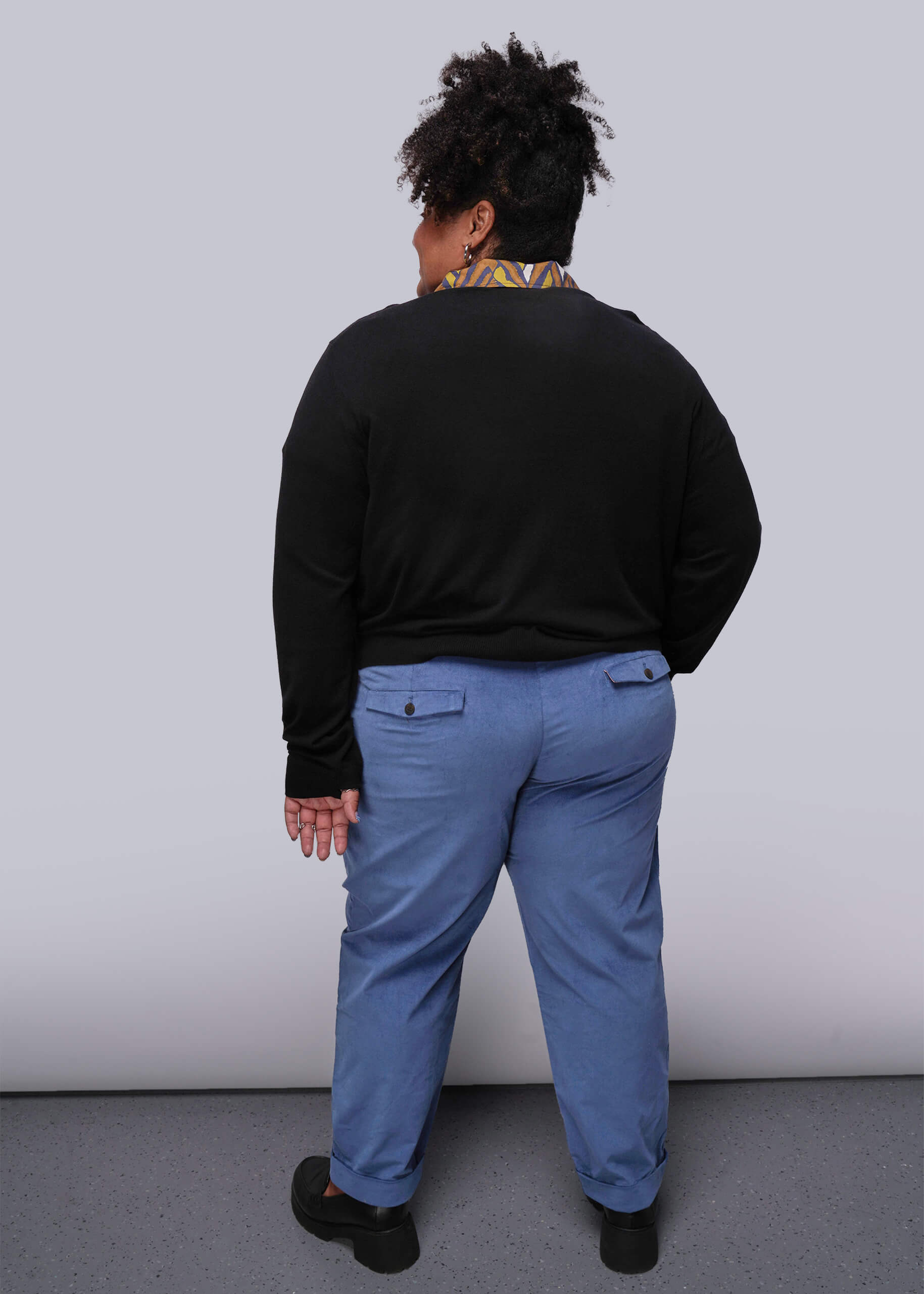 1X=Person wearing a black sweater and blue pants against a white wall