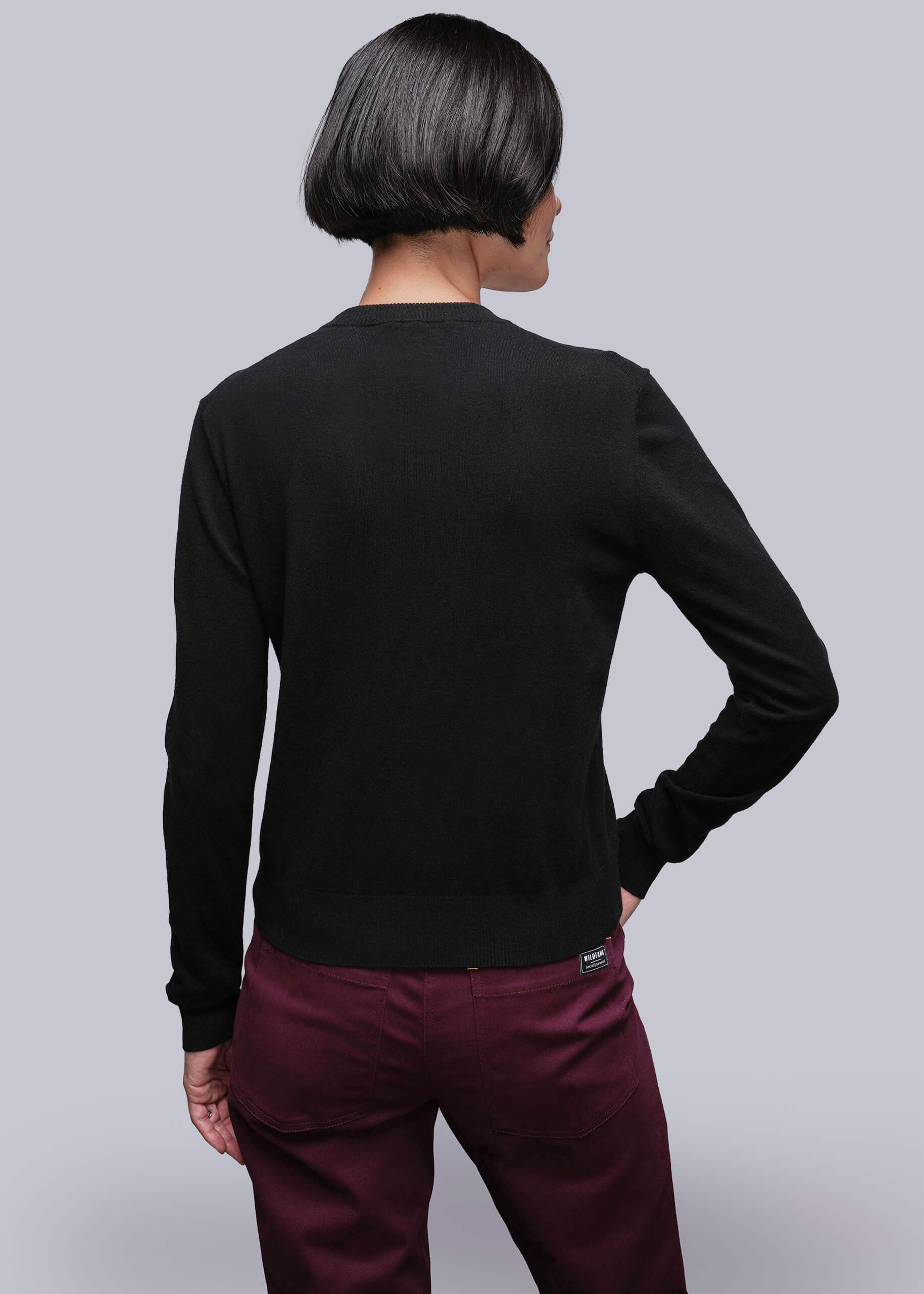 S=Person wearing a black long-sleeve sweater and maroon pants against a light gray background