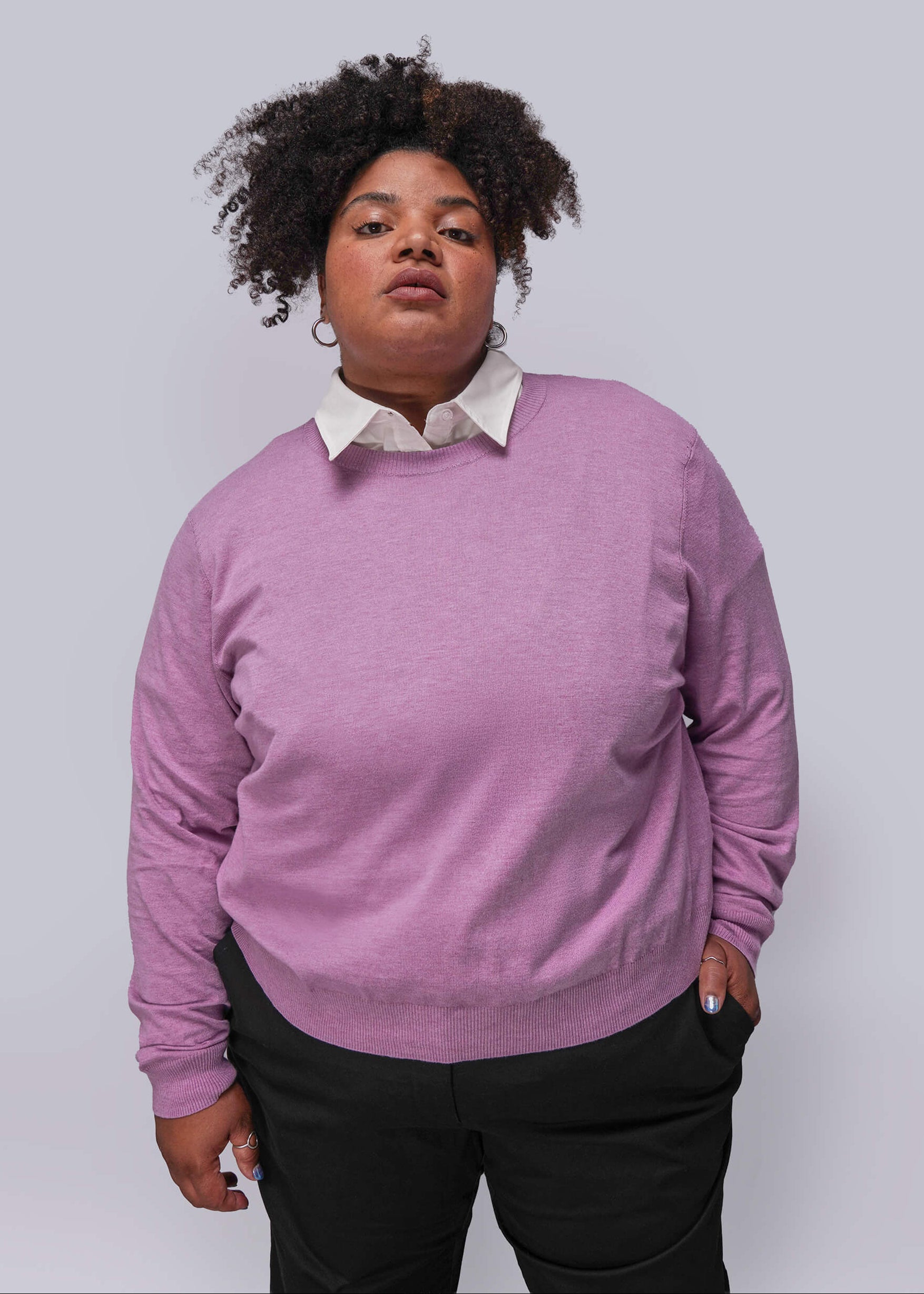 1X=Person wearing a pink sweater over a white shirt with black pants on a plain background
