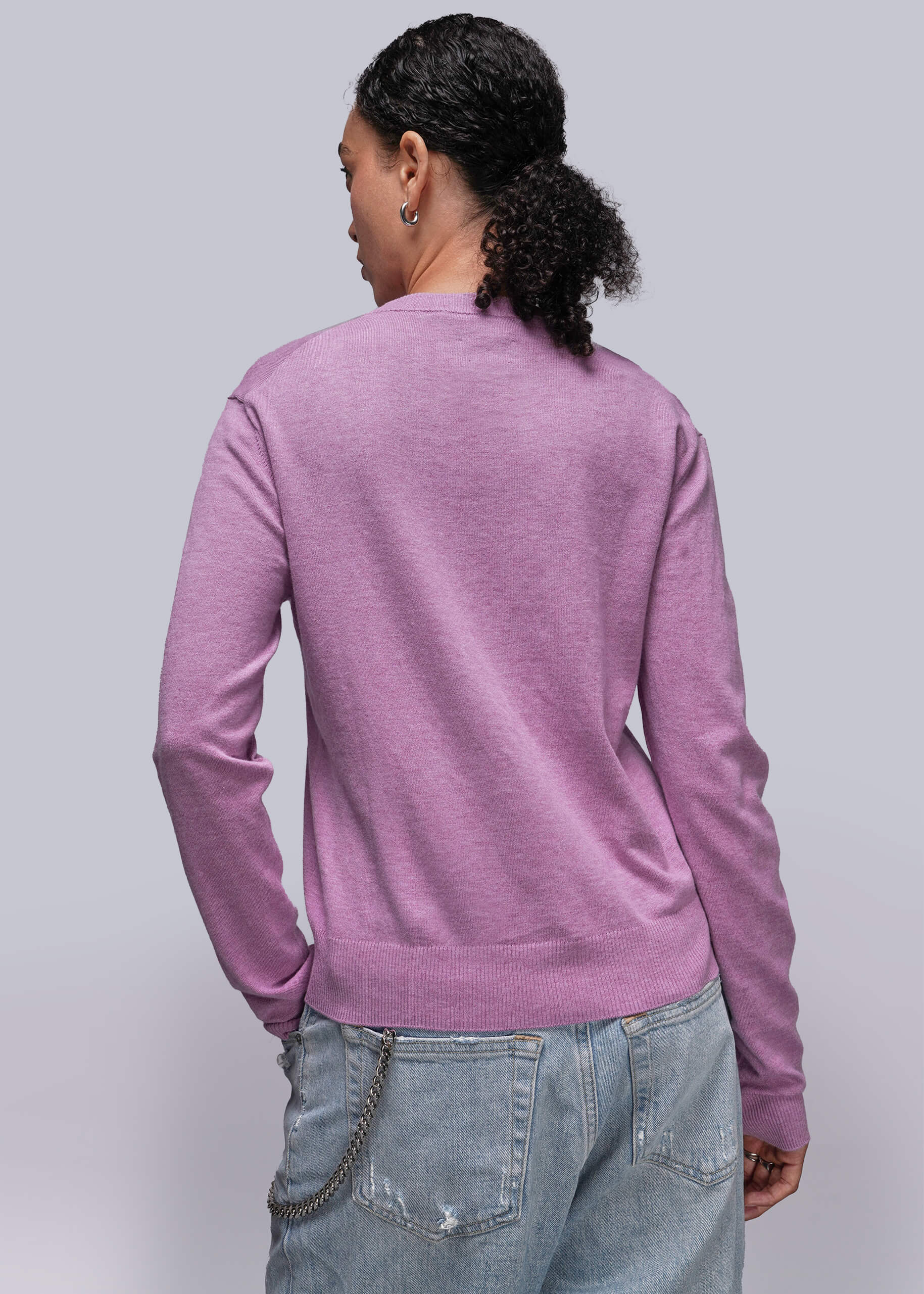 S=Person wearing a pink toned sweater and light blue jeans against a plain background