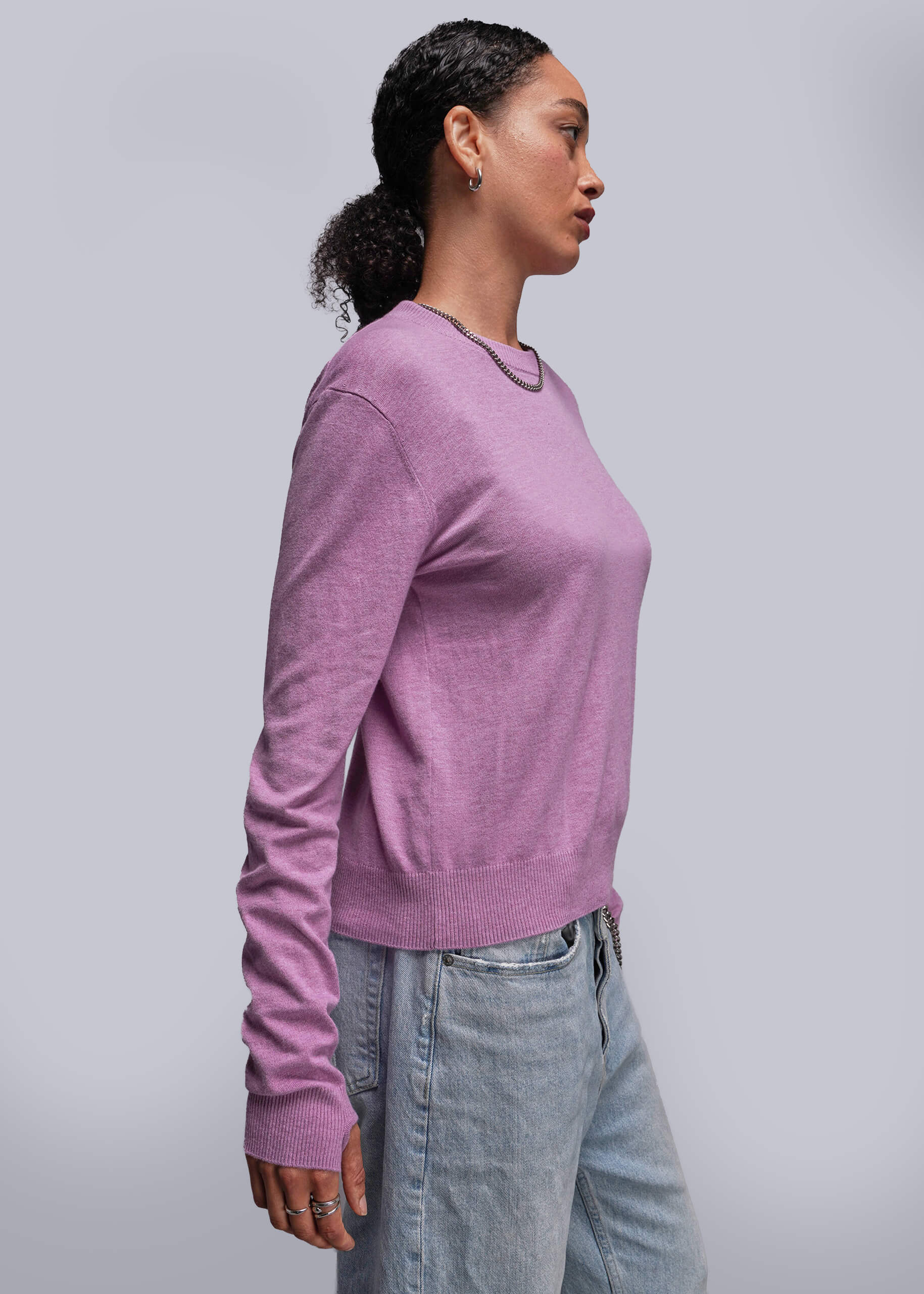 S=Person wearing a pink sweater and light blue jeans against a plain background