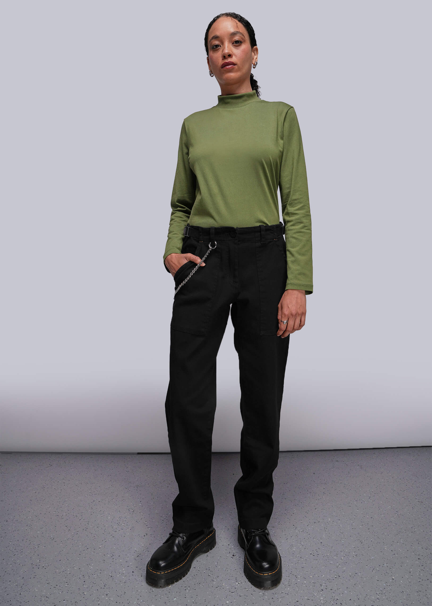 S=Person wearing a green long-sleeve top and black pants against a plain background