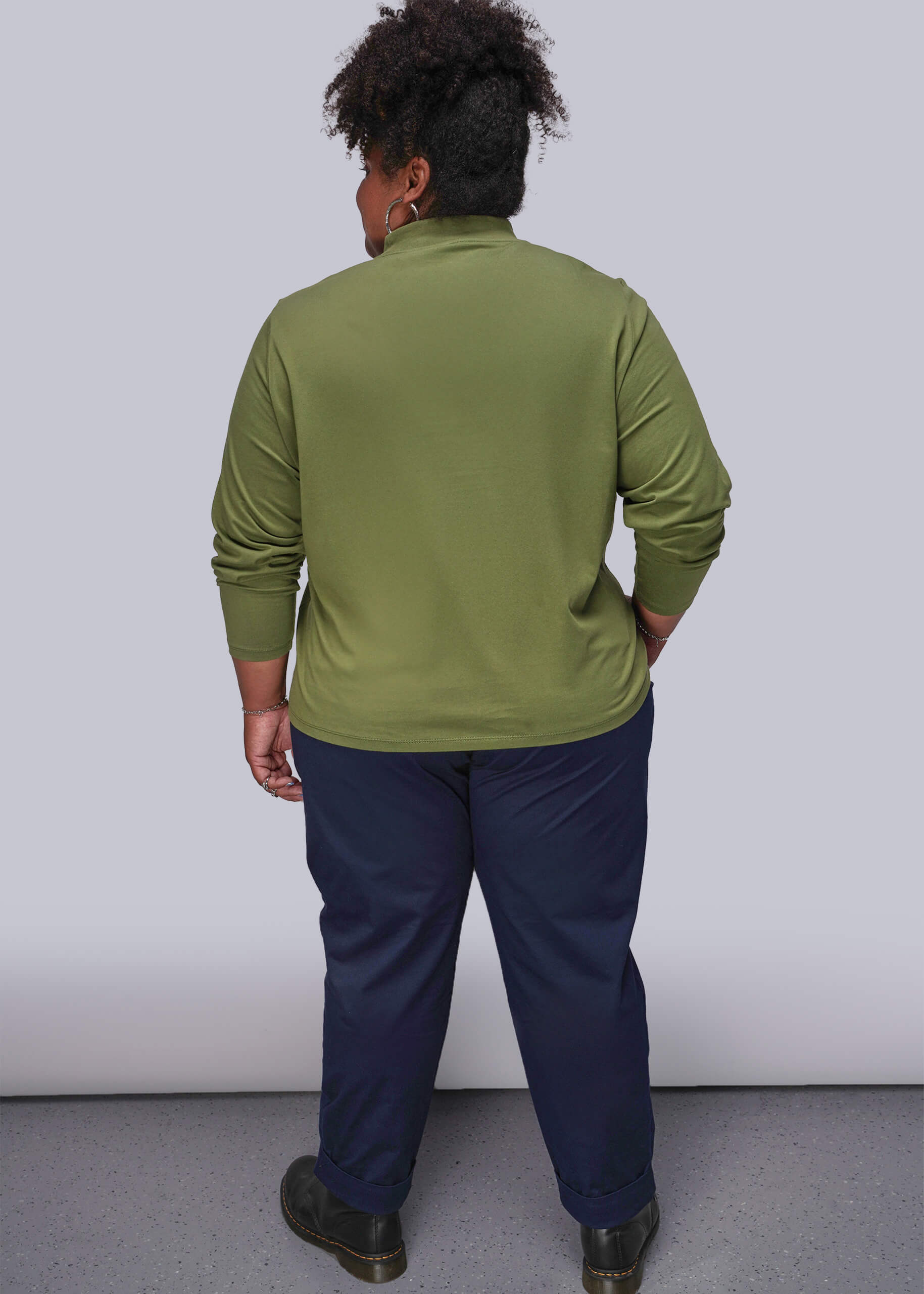 1X=Back of person wearing a green long-sleeve shirt and navy pants against a white background
