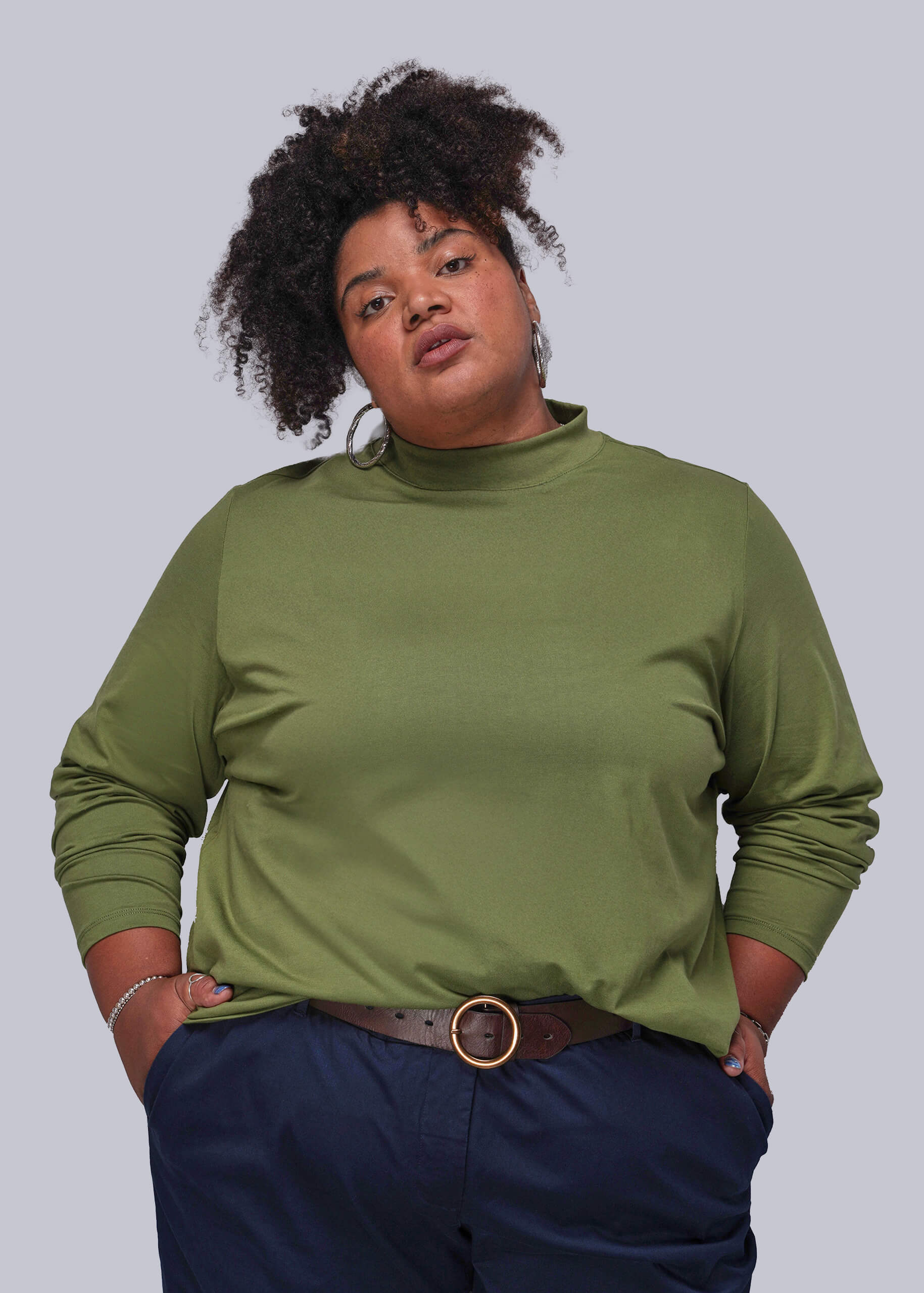 1X=Person wearing a green mock-neck top and navy pants on a white background
