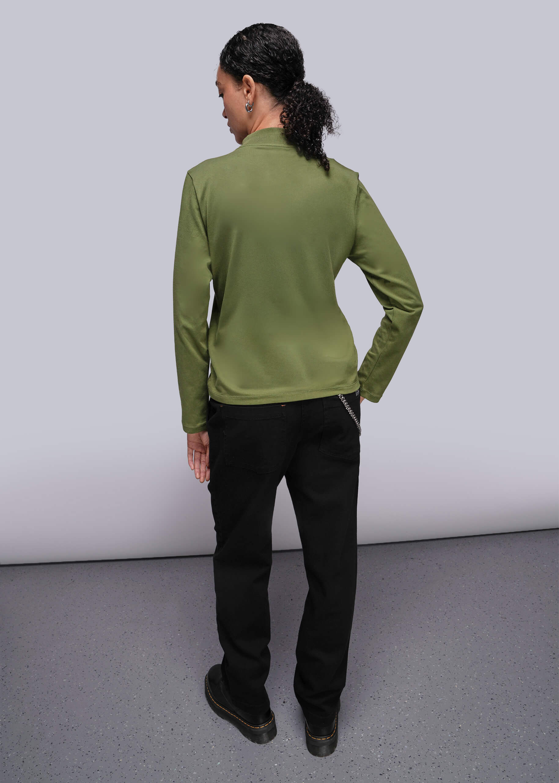 S=Person wearing a green long sleeve shirt and black pants on a plain background