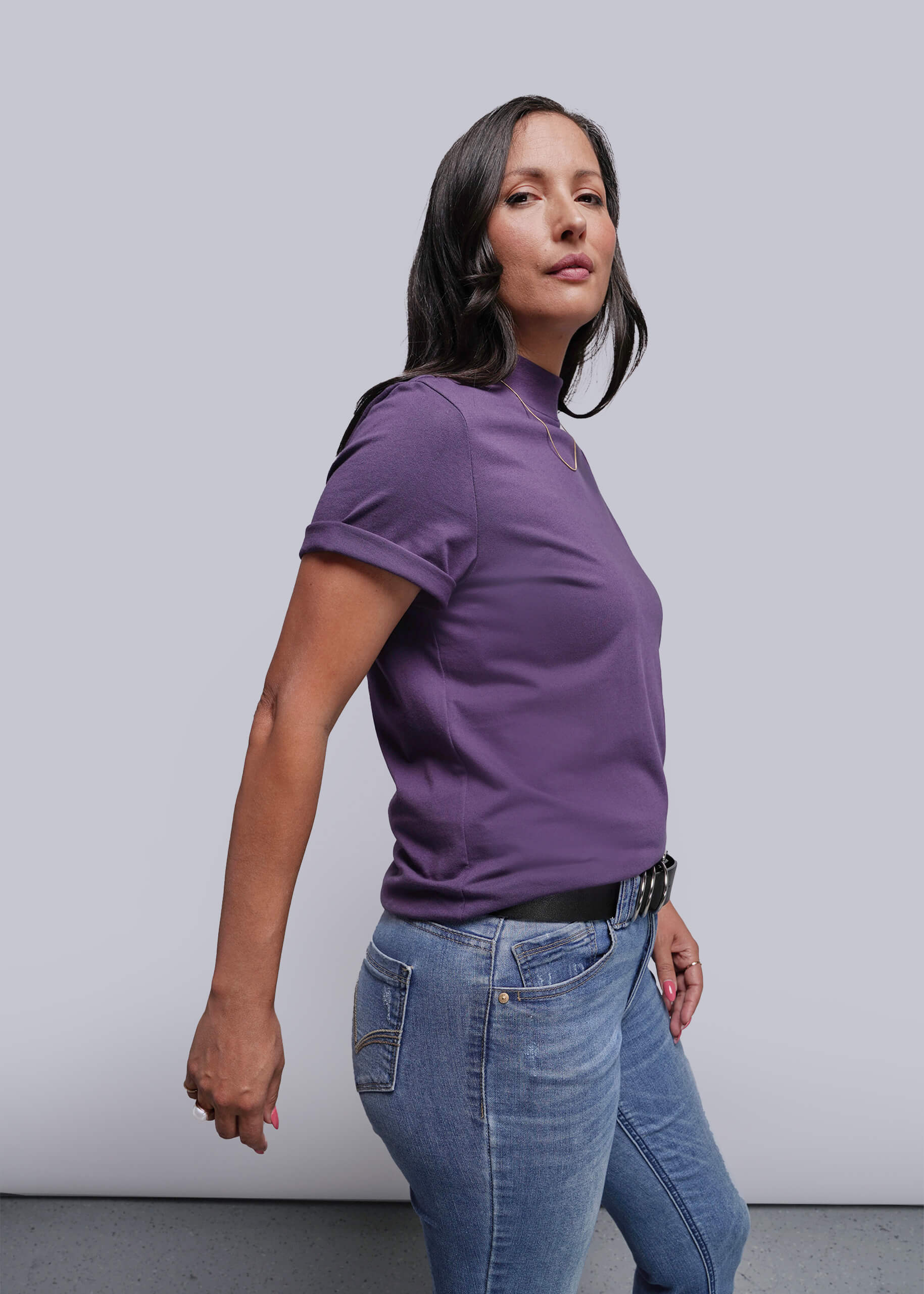 S=Woman wearing a purple shirt and blue jeans against a plain background