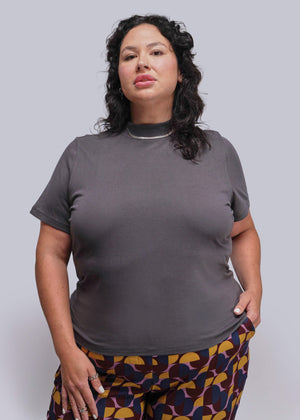 1X=Woman wearing a gray t-shirt and patterned pants against a plain background
