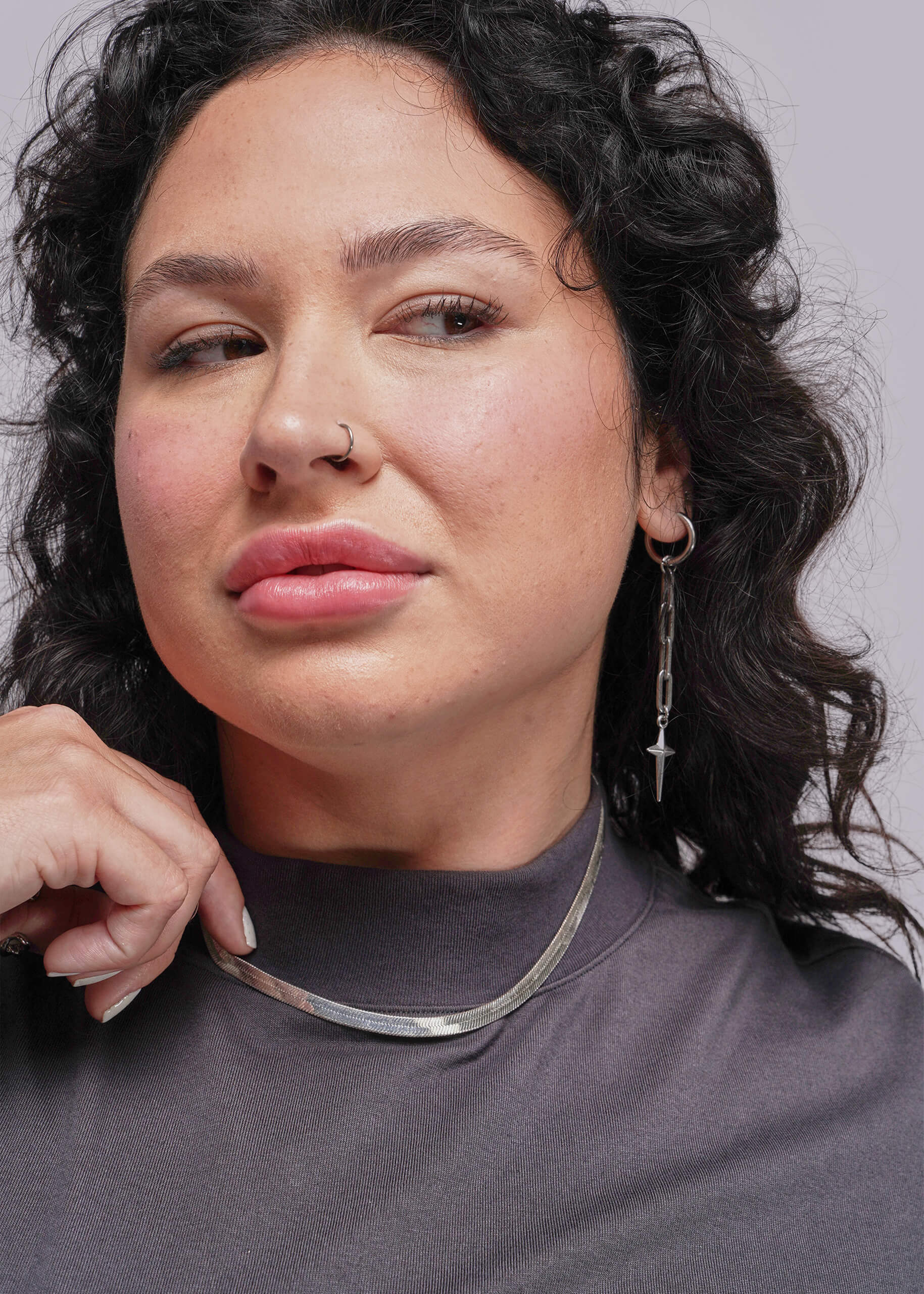 1X=Woman wearing a silver necklace against a neutral background