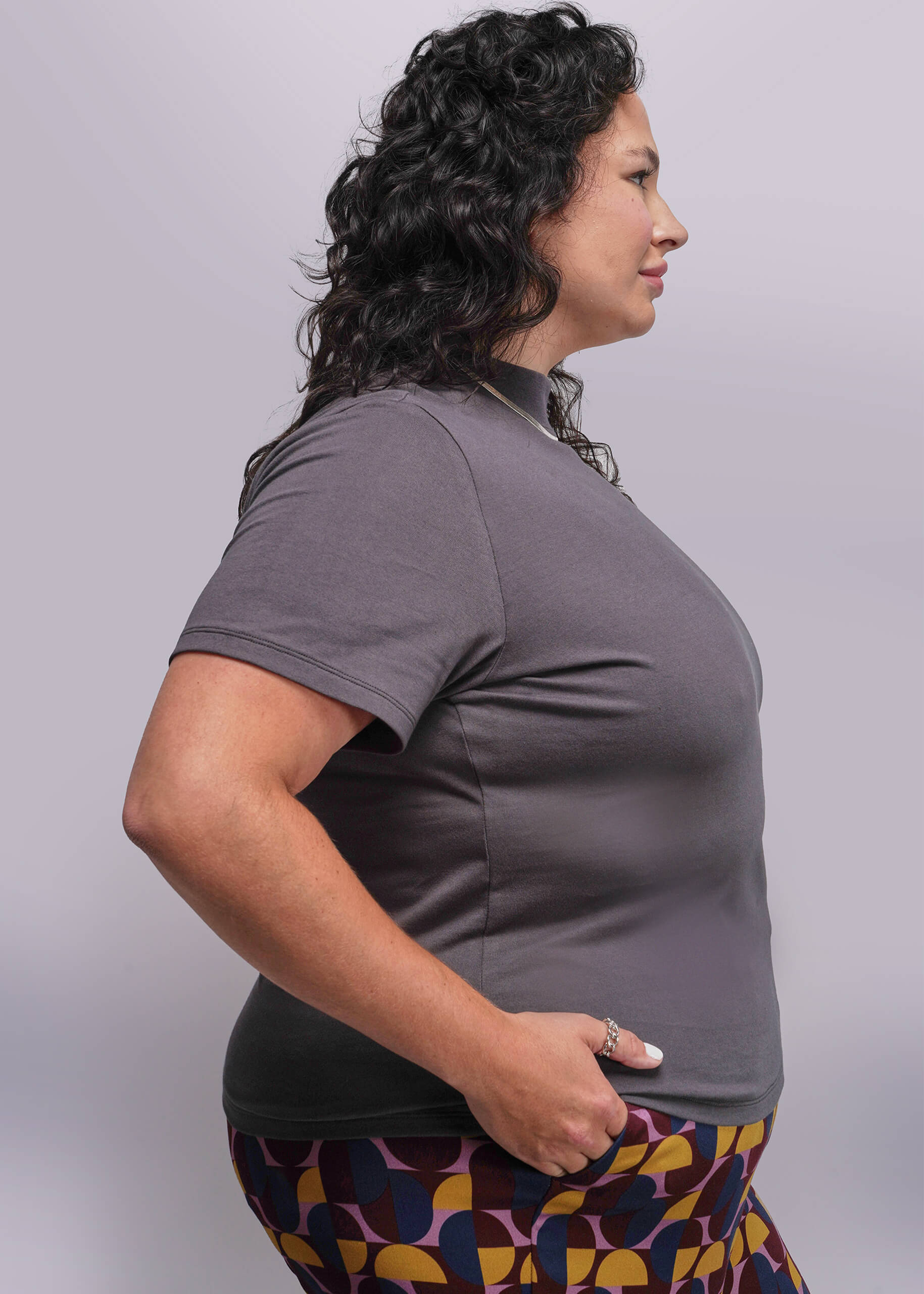 1X=Woman wearing a gray shirt and patterned pants against a plain background