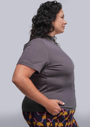 1X=Woman wearing a gray shirt and patterned pants against a plain background