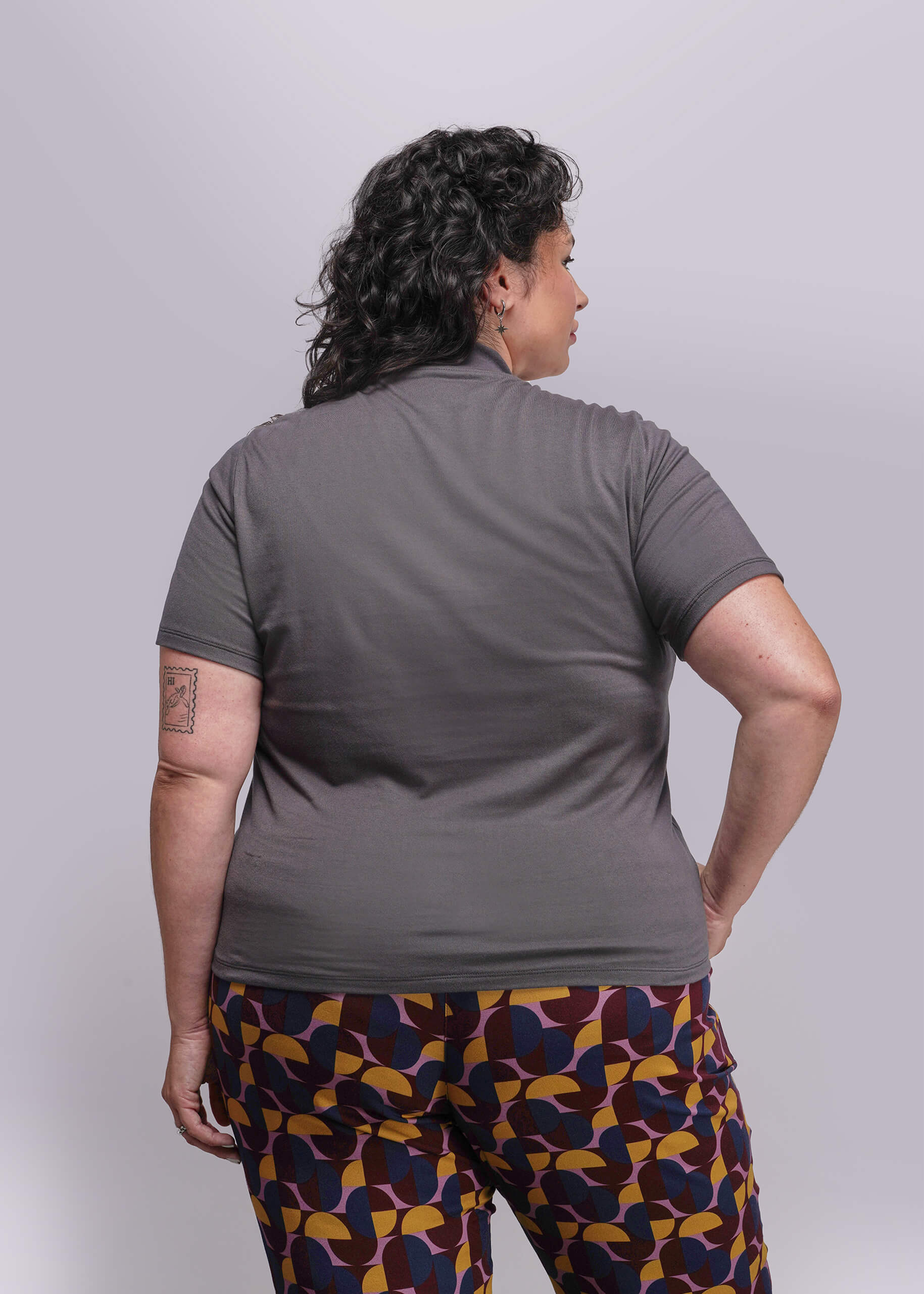 1X=Person wearing a gray shirt and patterned pants on a plain background