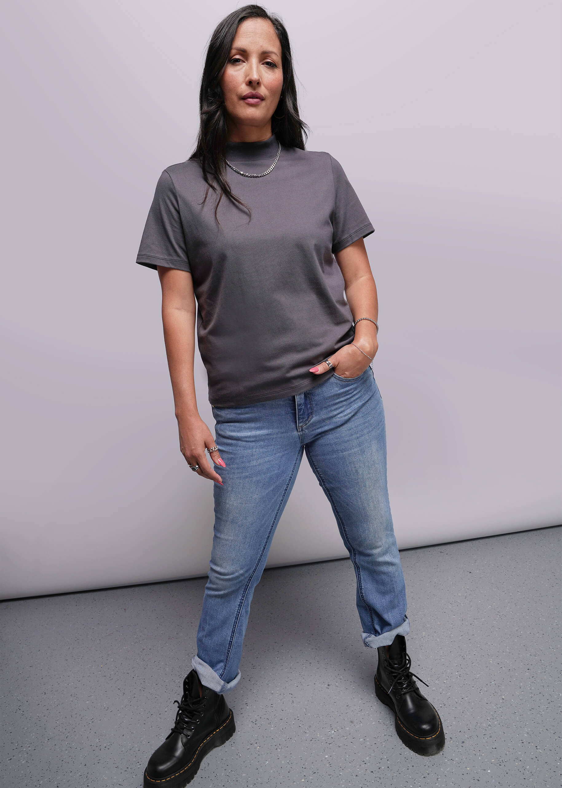 S=Person wearing a gray t-shirt, blue jeans, and black boots against a plain background