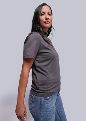 S=Woman wearing a gray t-shirt and blue jeans against a plain background