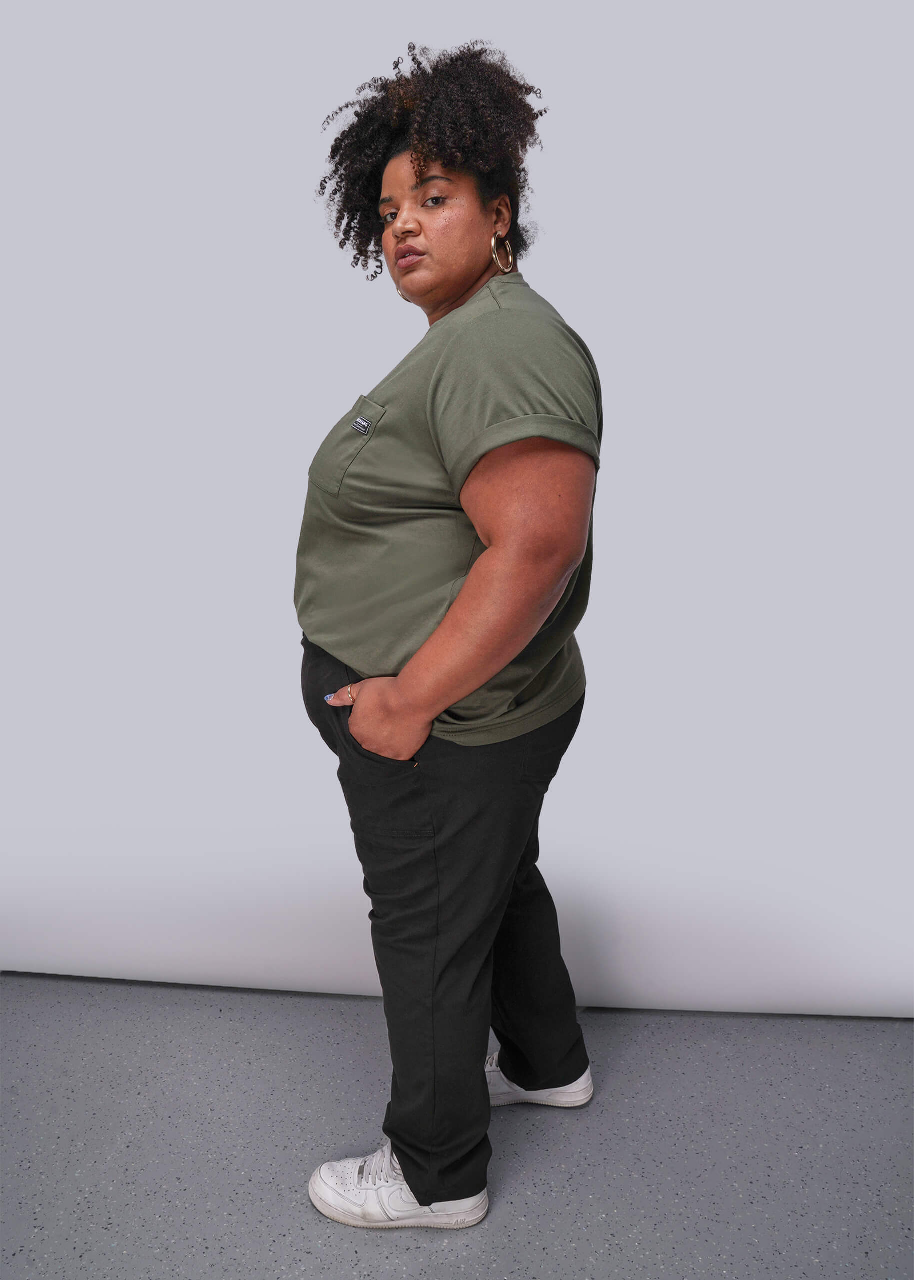 1X=Person wearing a green shirt and black pants against a plain background