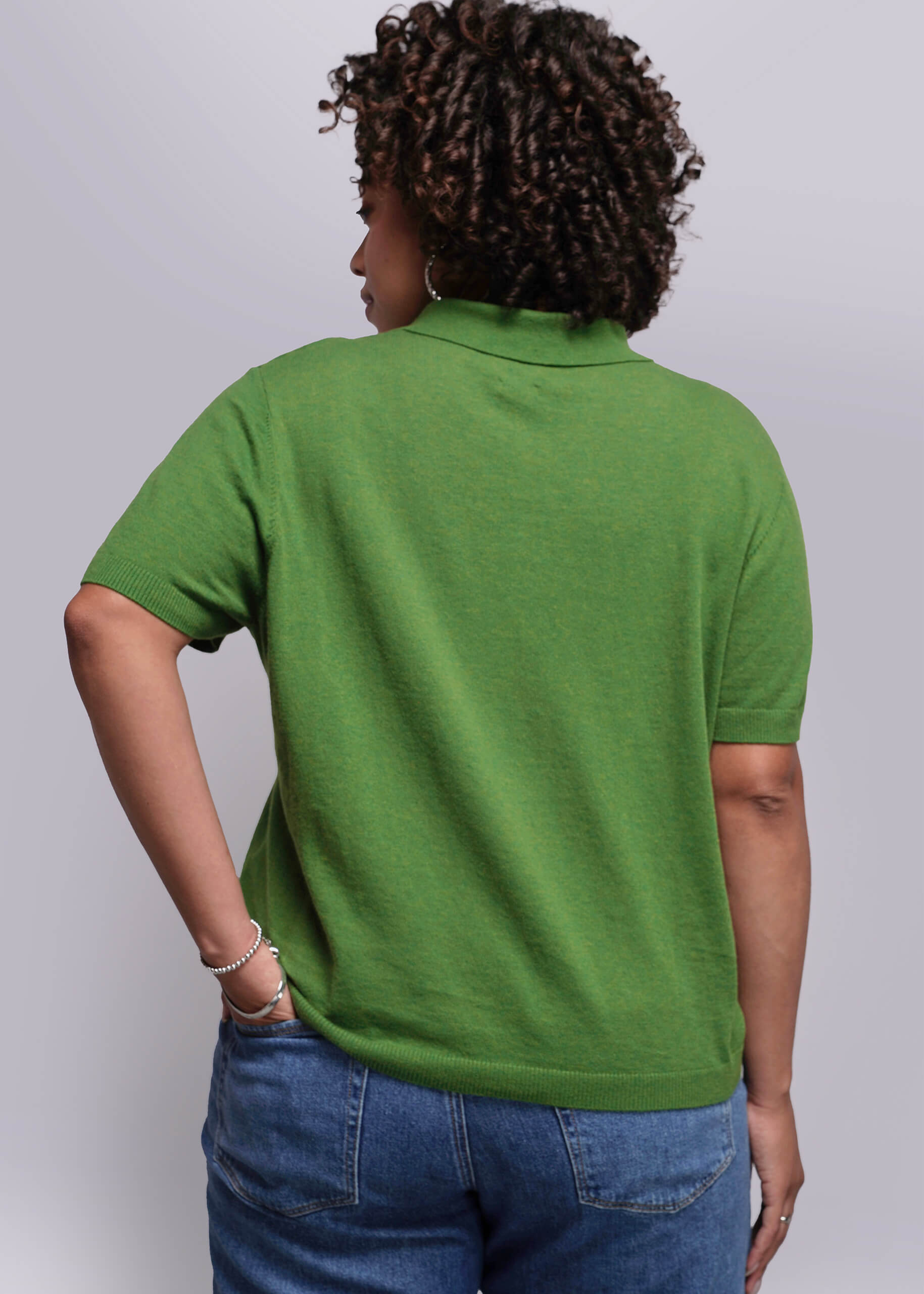 1X=Person wearing a green polo shirt and blue jeans against a plain background