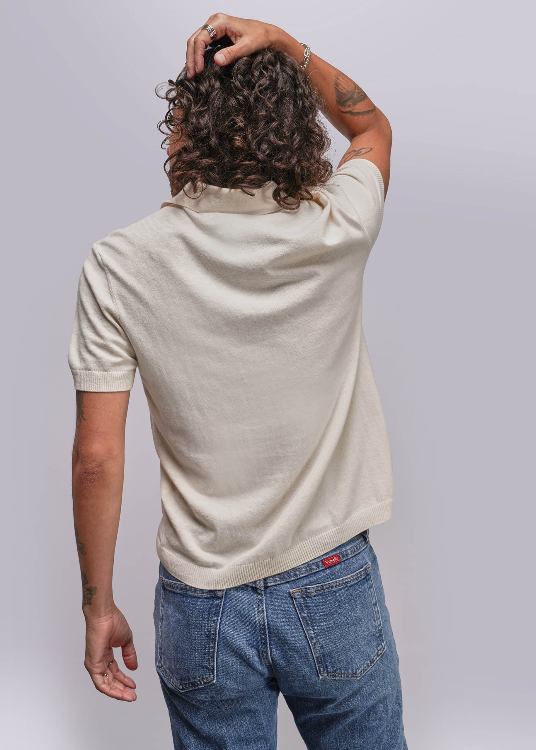 S=Person wearing a beige polo shirt and blue jeans against a plain background