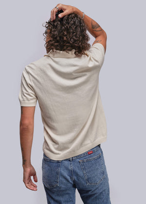S=Person wearing a beige polo shirt and blue jeans against a plain background