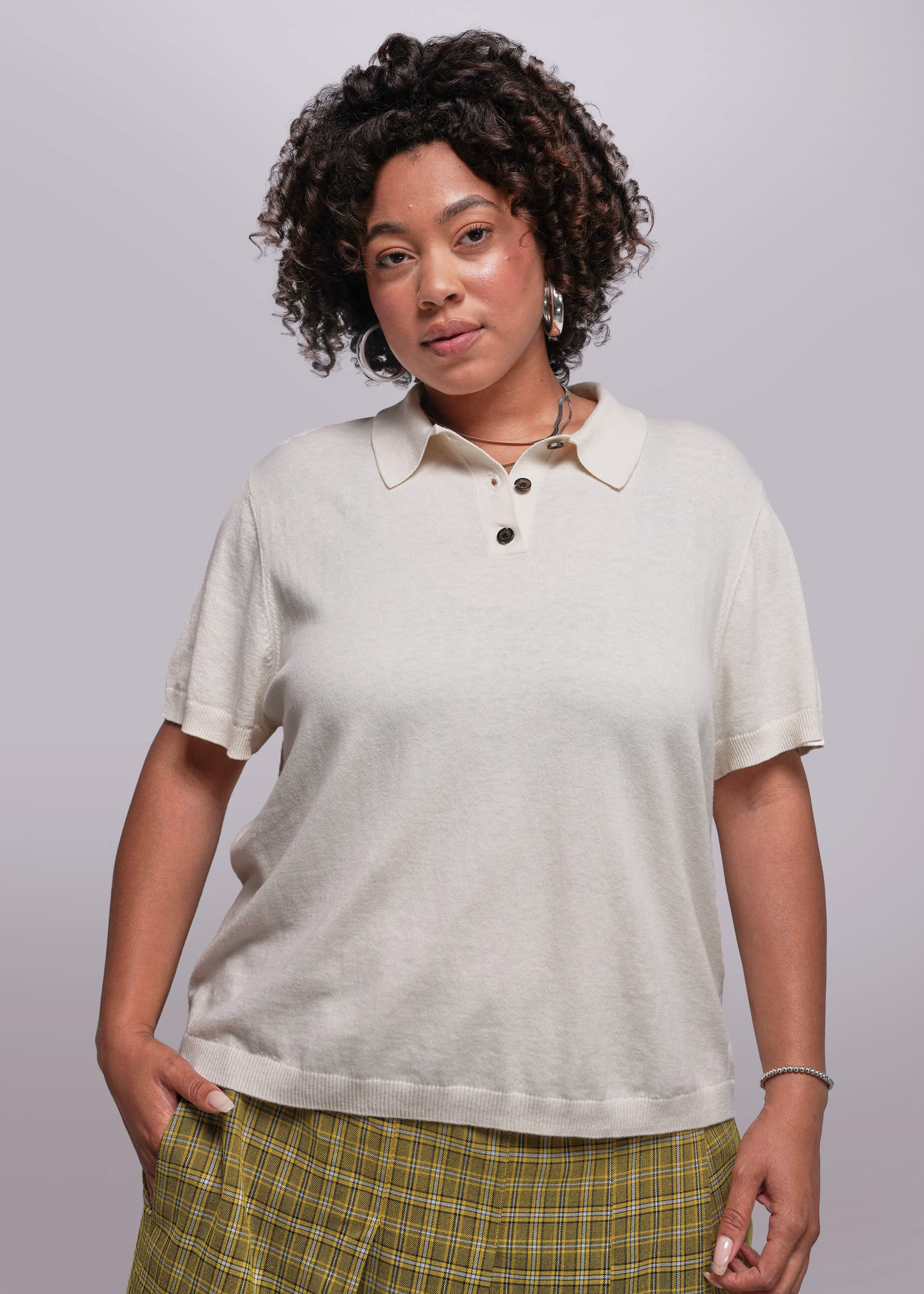 1X=Woman wearing a beige polo shirt and plaid pants against a plain background