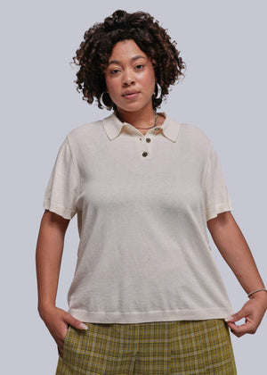 1X=Woman wearing a beige polo shirt and plaid pants against a plain background