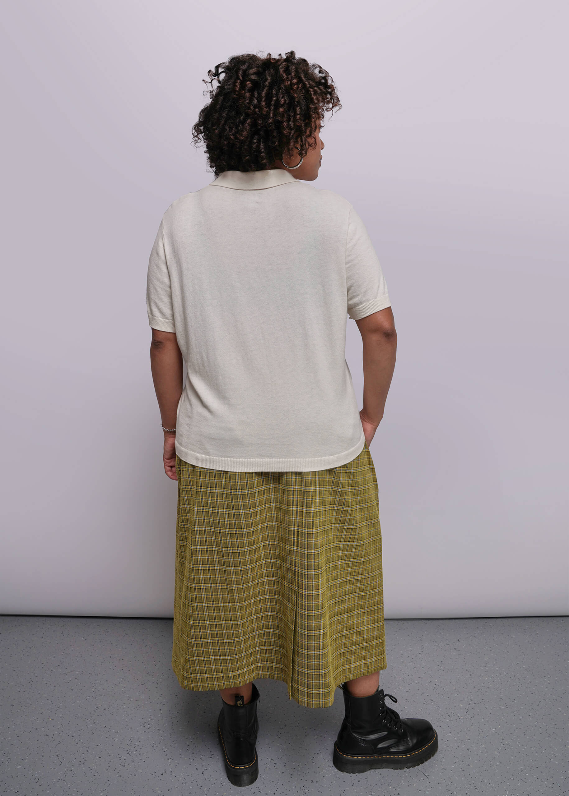 1X=Person wearing a white t-shirt and yellow plaid skirt against a plain background