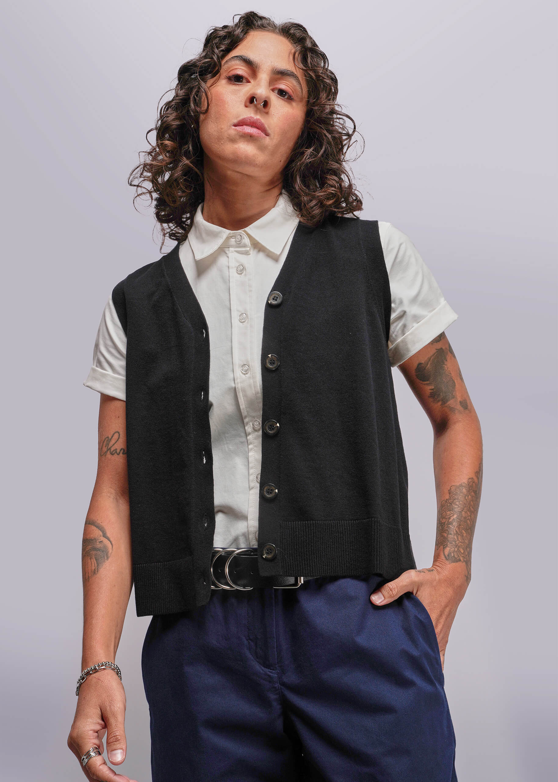 S=Person wearing a black vest over a white shirt with blue pants on a plain background