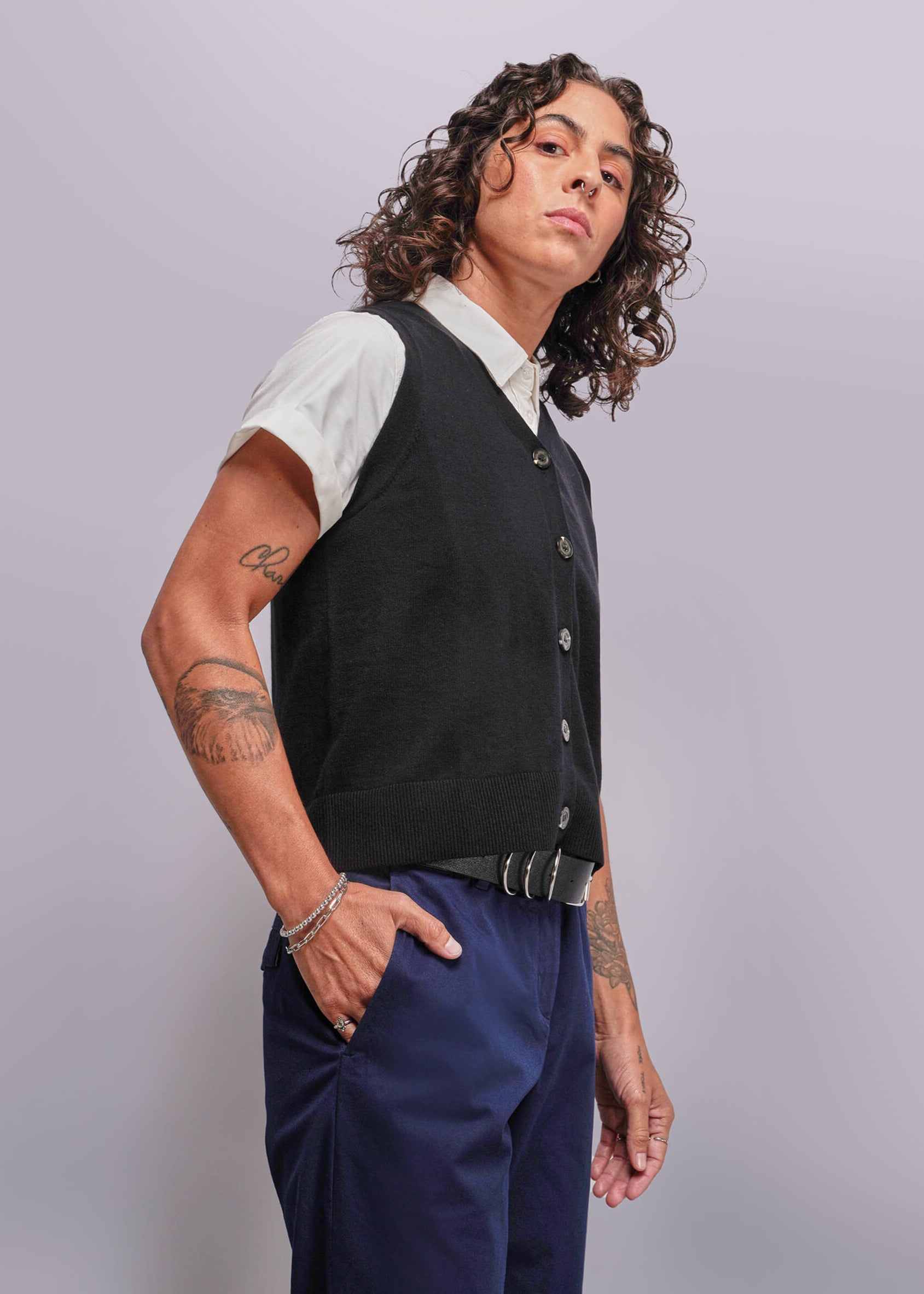 S=Person wearing a black vest over a white shirt with blue pants on a light gray background