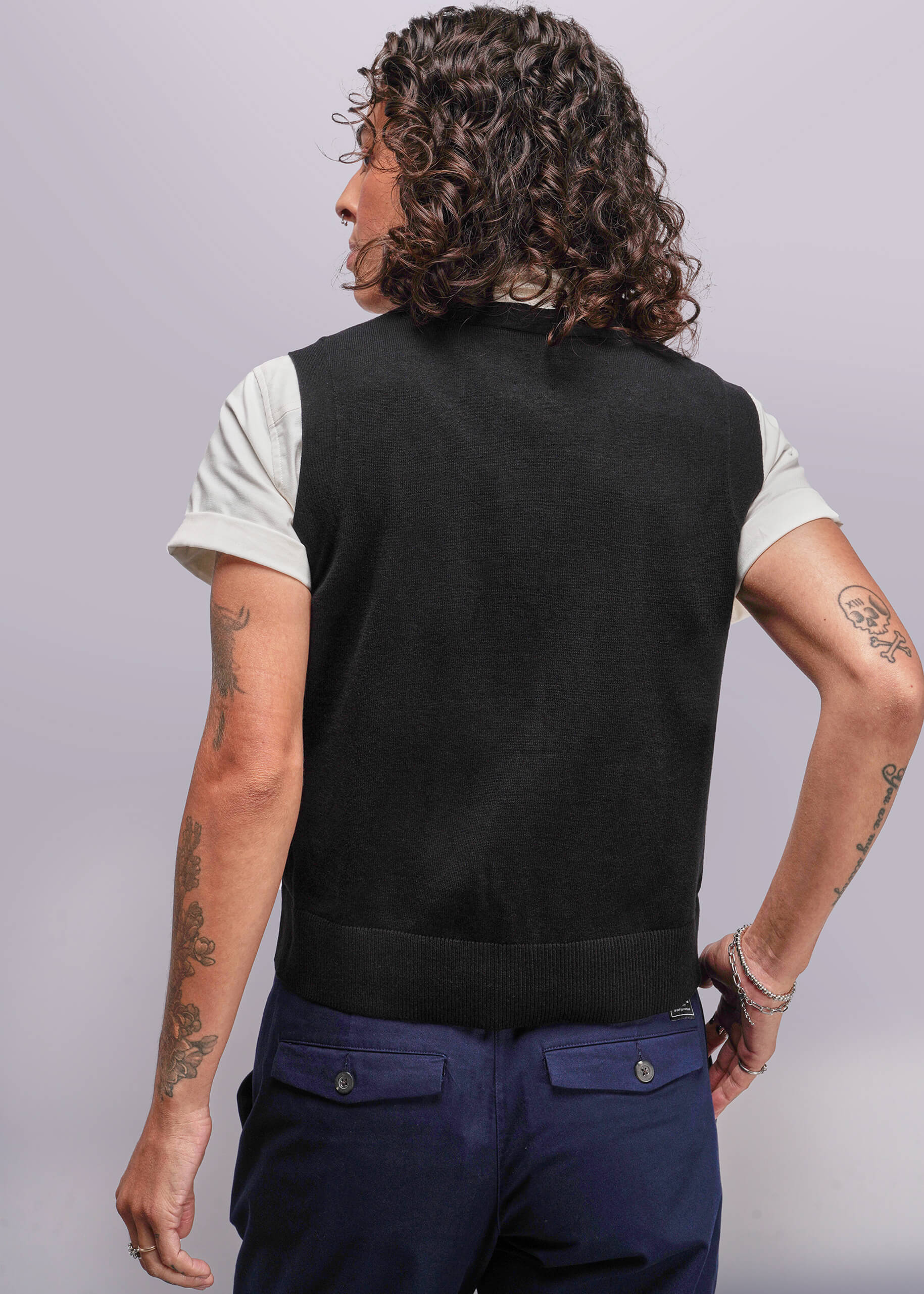 S=Person wearing a black vest over a white shirt with dark blue pants on a plain background