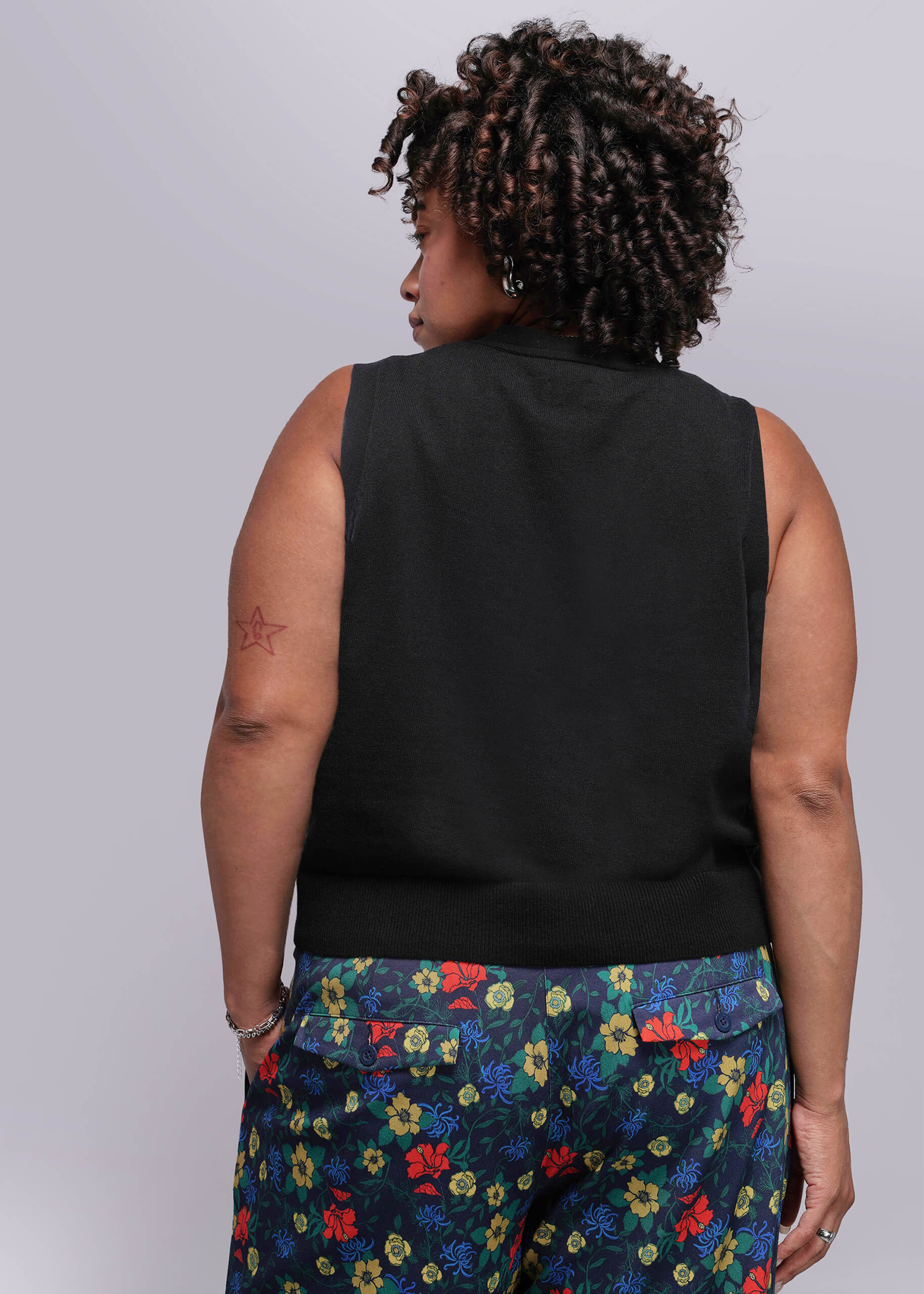 1X=Person wearing a black sleeveless top and colorful floral pants on a plain background