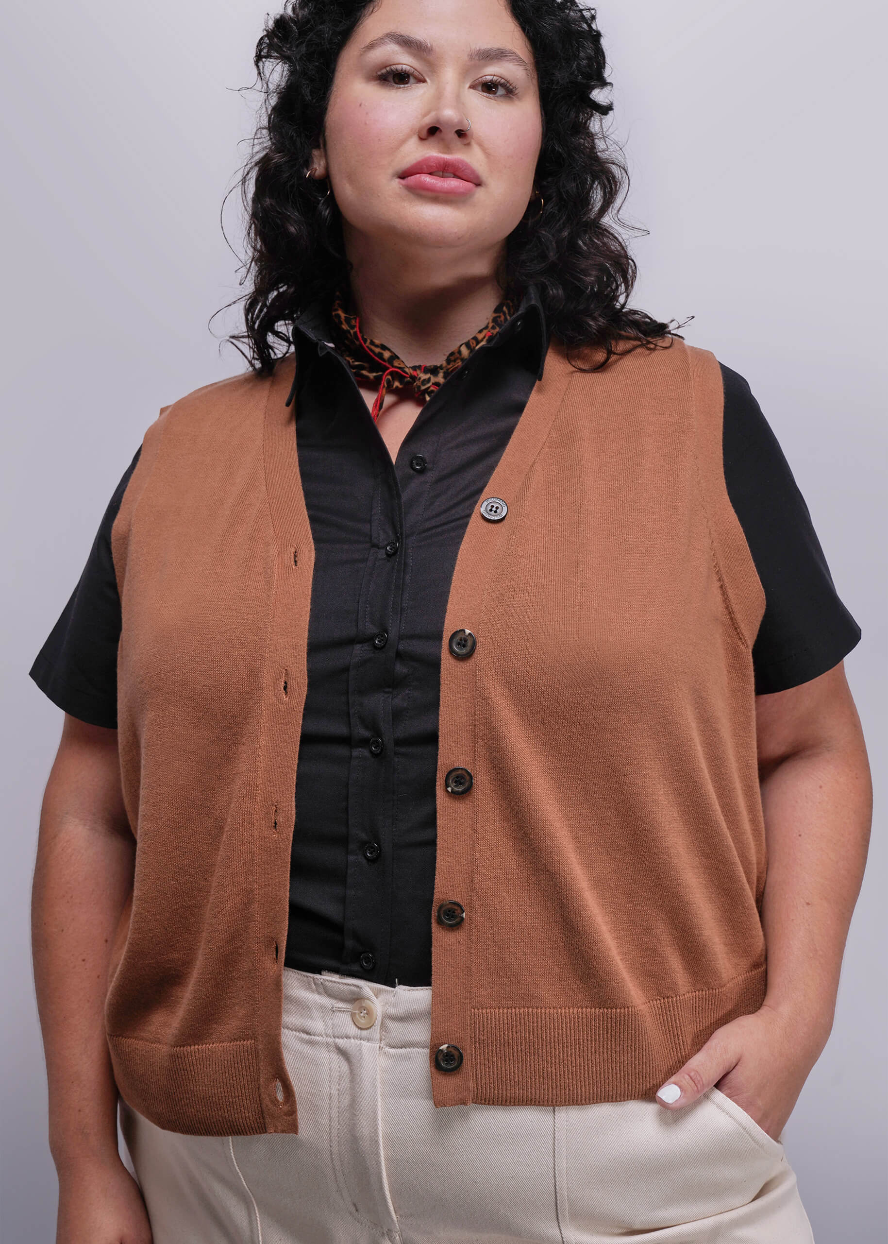1X=Person wearing a brown vest over a black shirt with a plain background